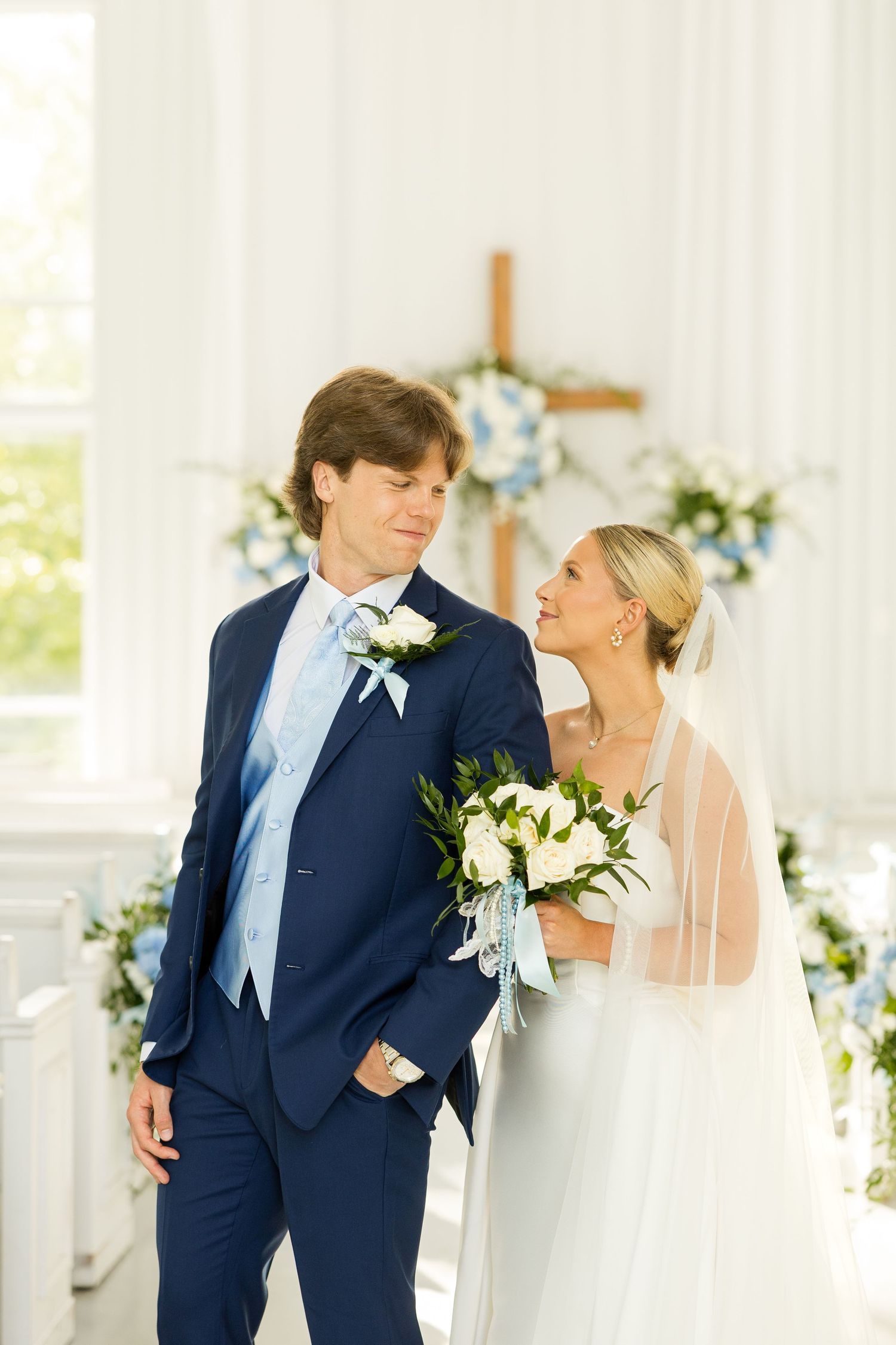 Romantic wedding moment captured in a white chapel with blue floral decorations.Cold Springs Events