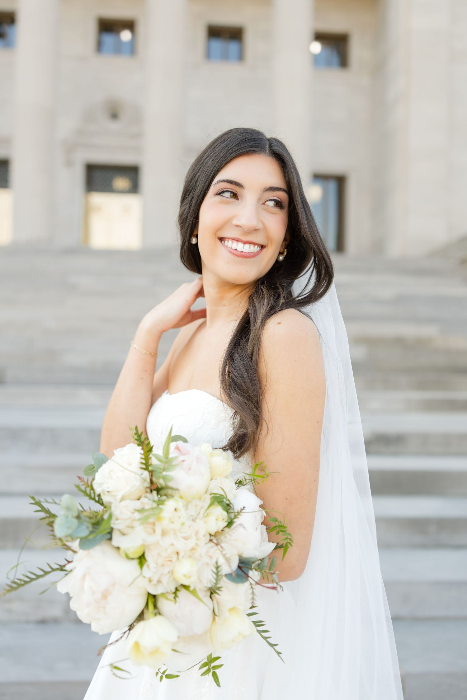 Classic bridal portrait with white bouquet against architectural backdrop.