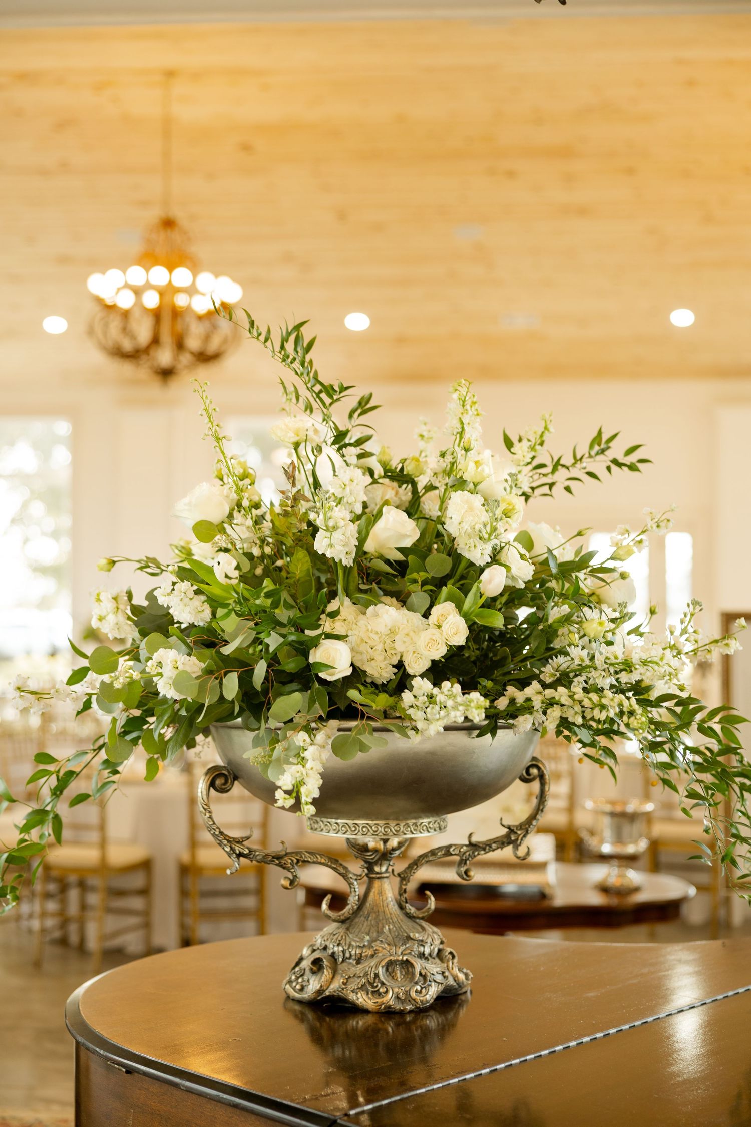 White floral centerpieces with greenery arranged on wooden tables in an elegant reception space.Marlgsate Plantation