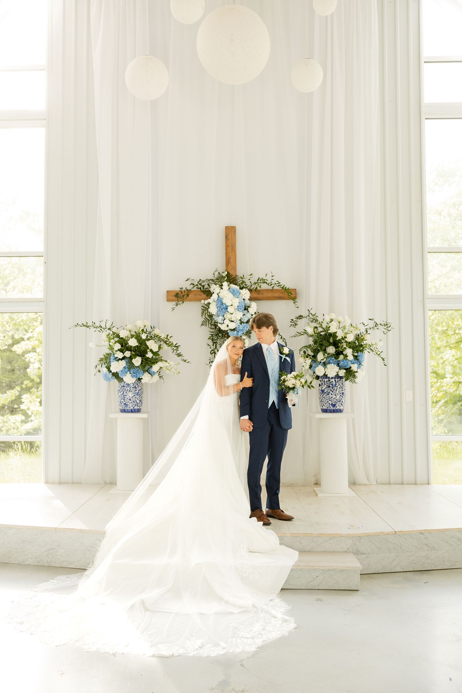 Wedding couple posing in an all-white chapel with blue and white floral arrangements. Cold Springs Events