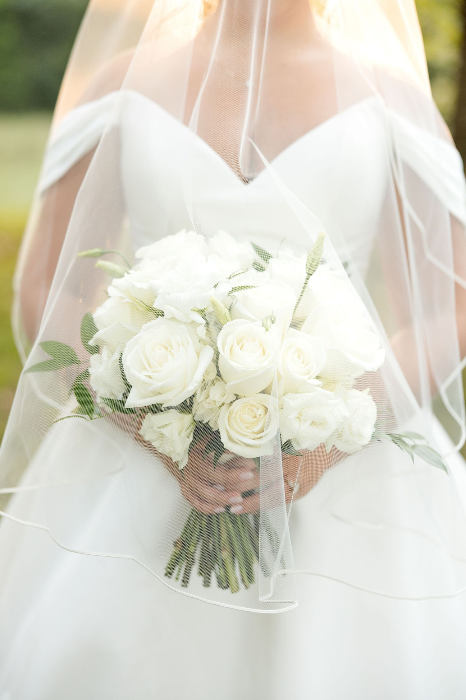 A classic white bridal bouquet of roses is held against a flowing white wedding gown.