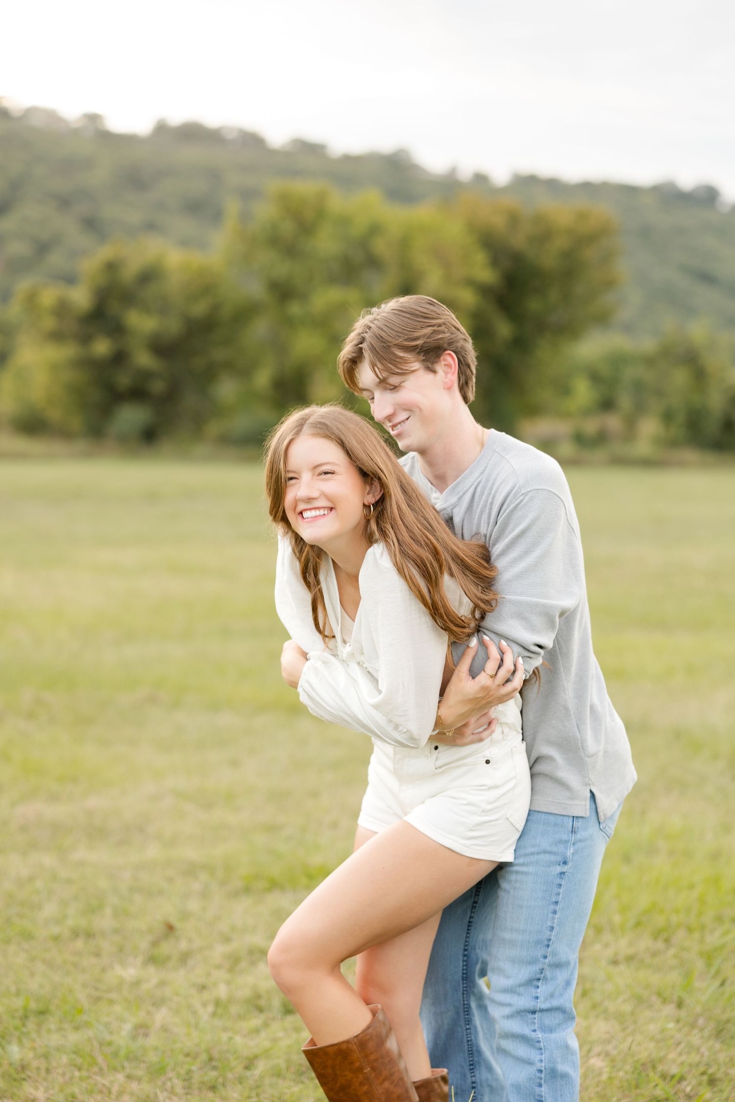 A joyful couple laughing and playing together in a grassy field on a bright afternoon.