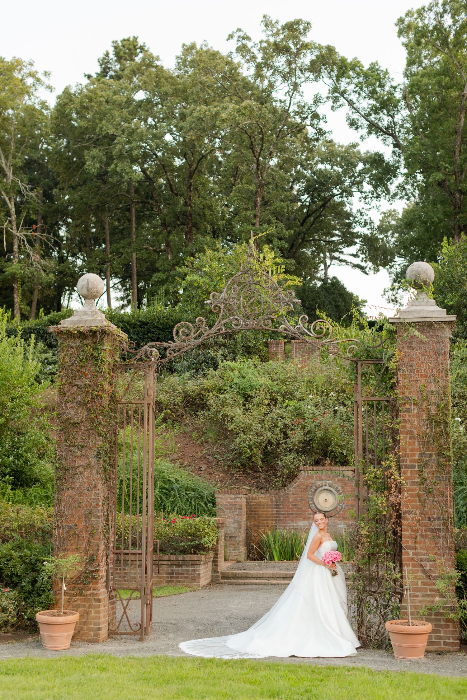 A romantic bridal photo series captured by a brick garden gate with ornate ironwork and lush greenery.