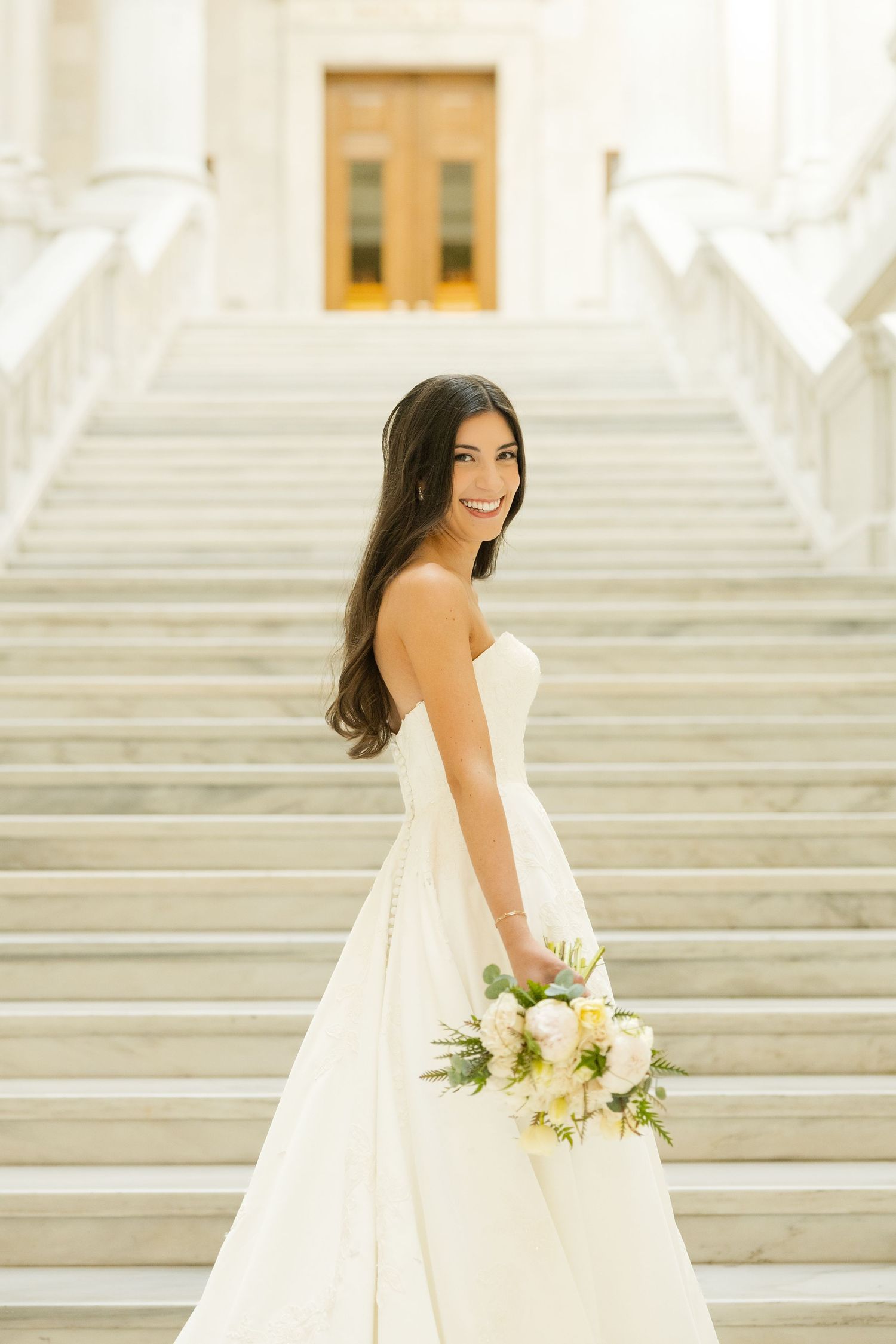 Elegant bridal portrait session on grand white marble steps with a flowing white wedding gown and delicate bouquet.
