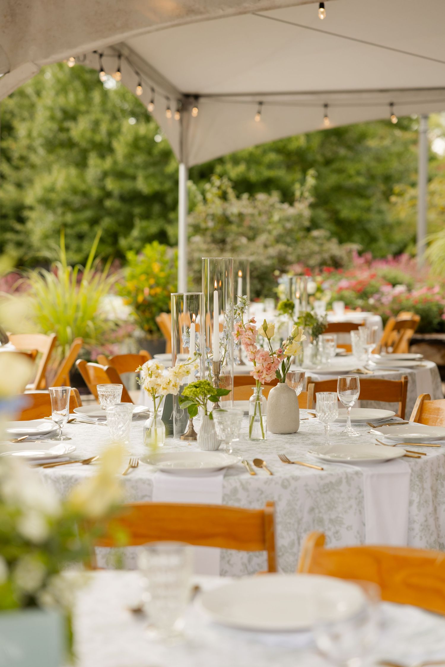 Elegant wedding reception tables set with white linens and wooden chairs under a tent outdoors.Botanical Gardens of the Ozarks
