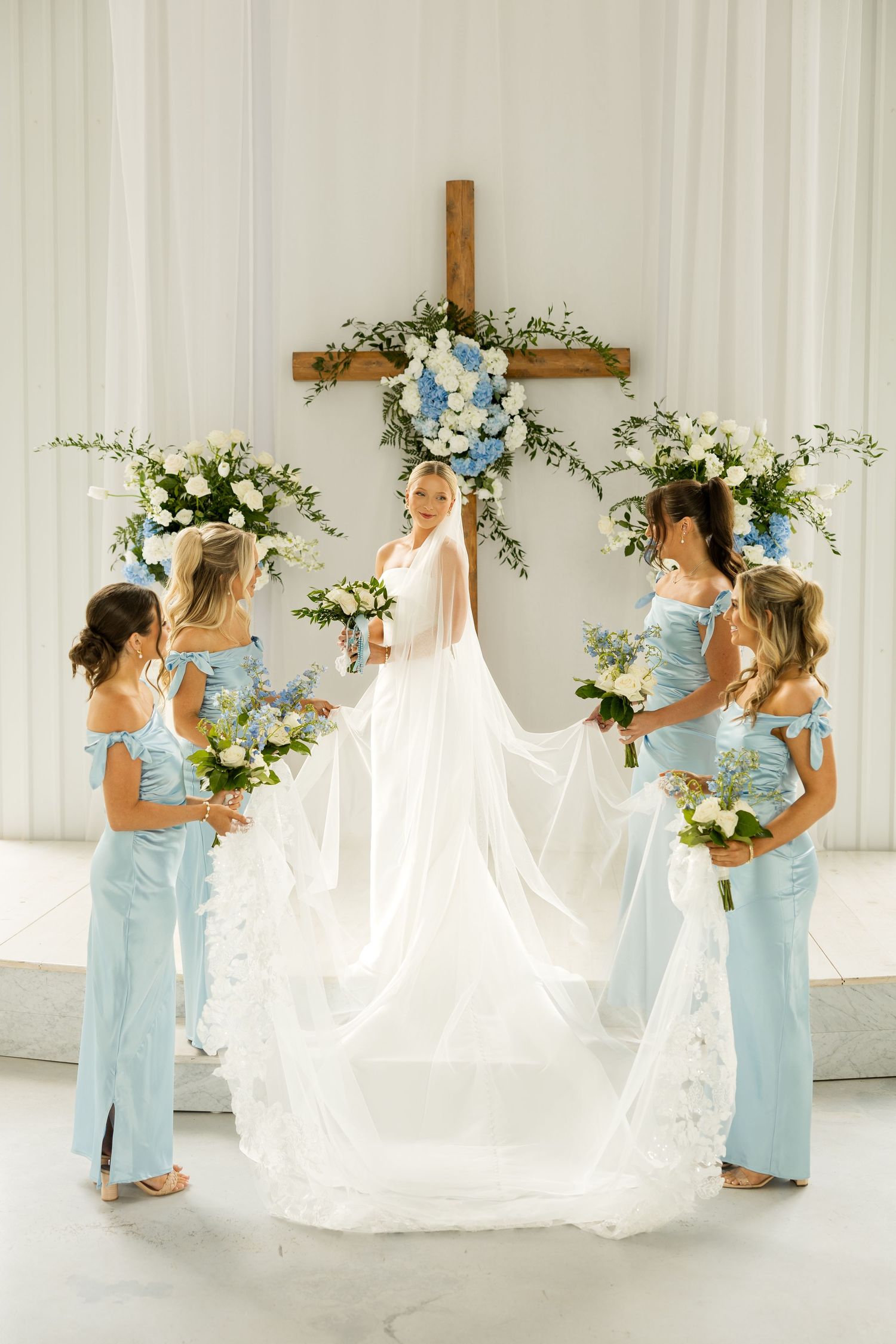 Bridesmaids in light blue dresses helping with wedding dress train in white chapel.Cold Springs Events