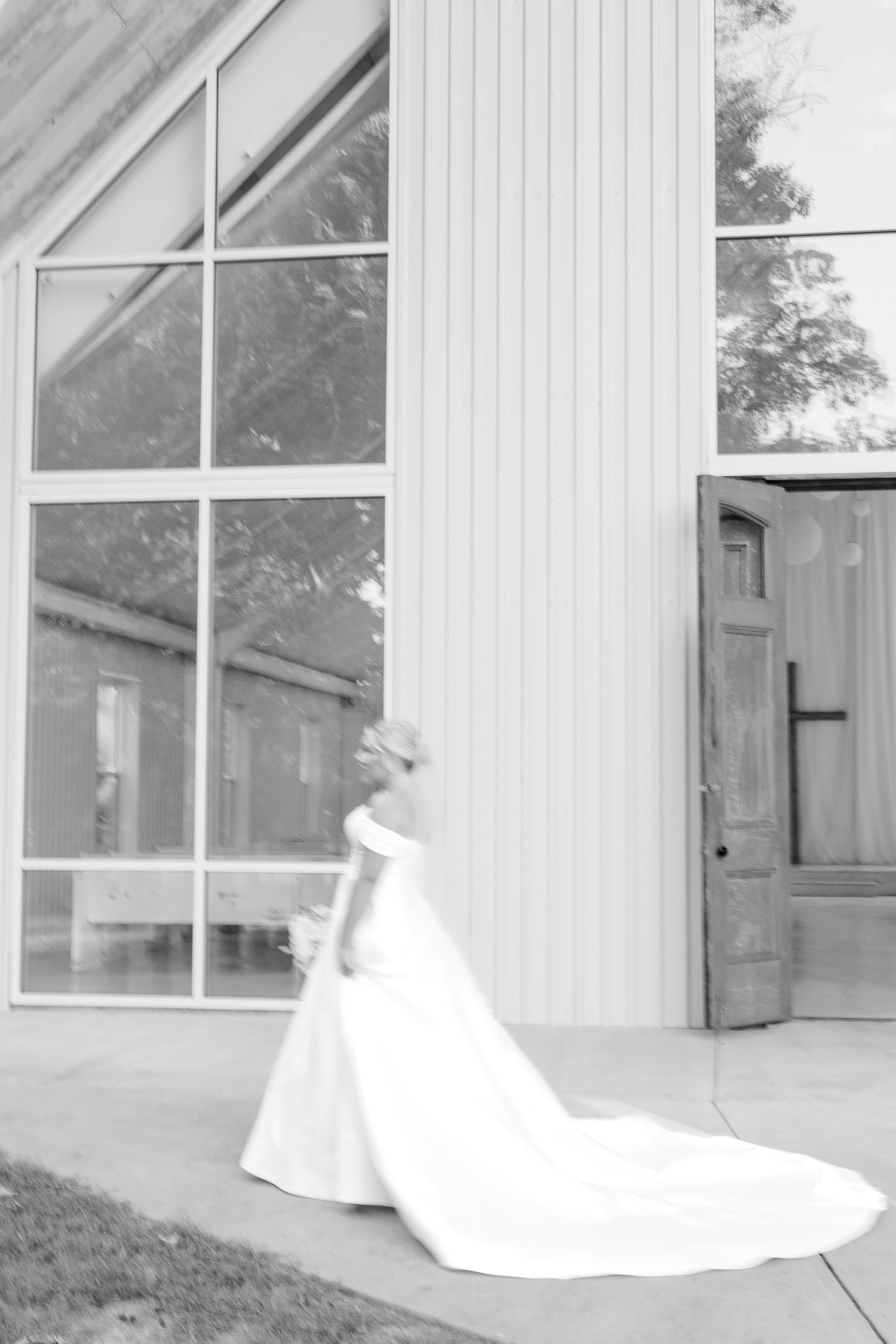 A flowing white wedding dress creates an elegant silhouette against a white chapel exterior with windows.
