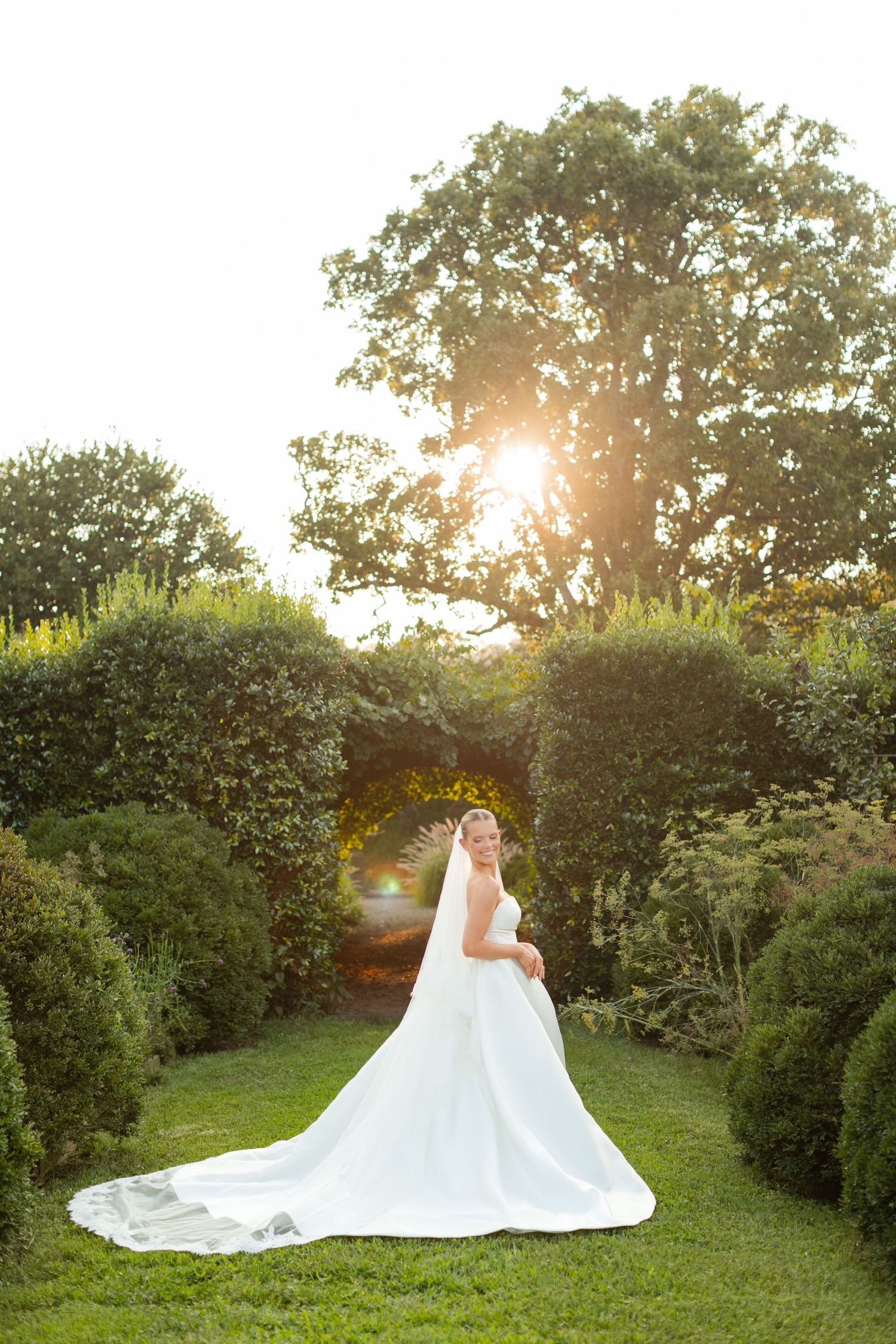 An elegant bridal gown with a cathedral train spreads beautifully across a garden pathway at golden hour.