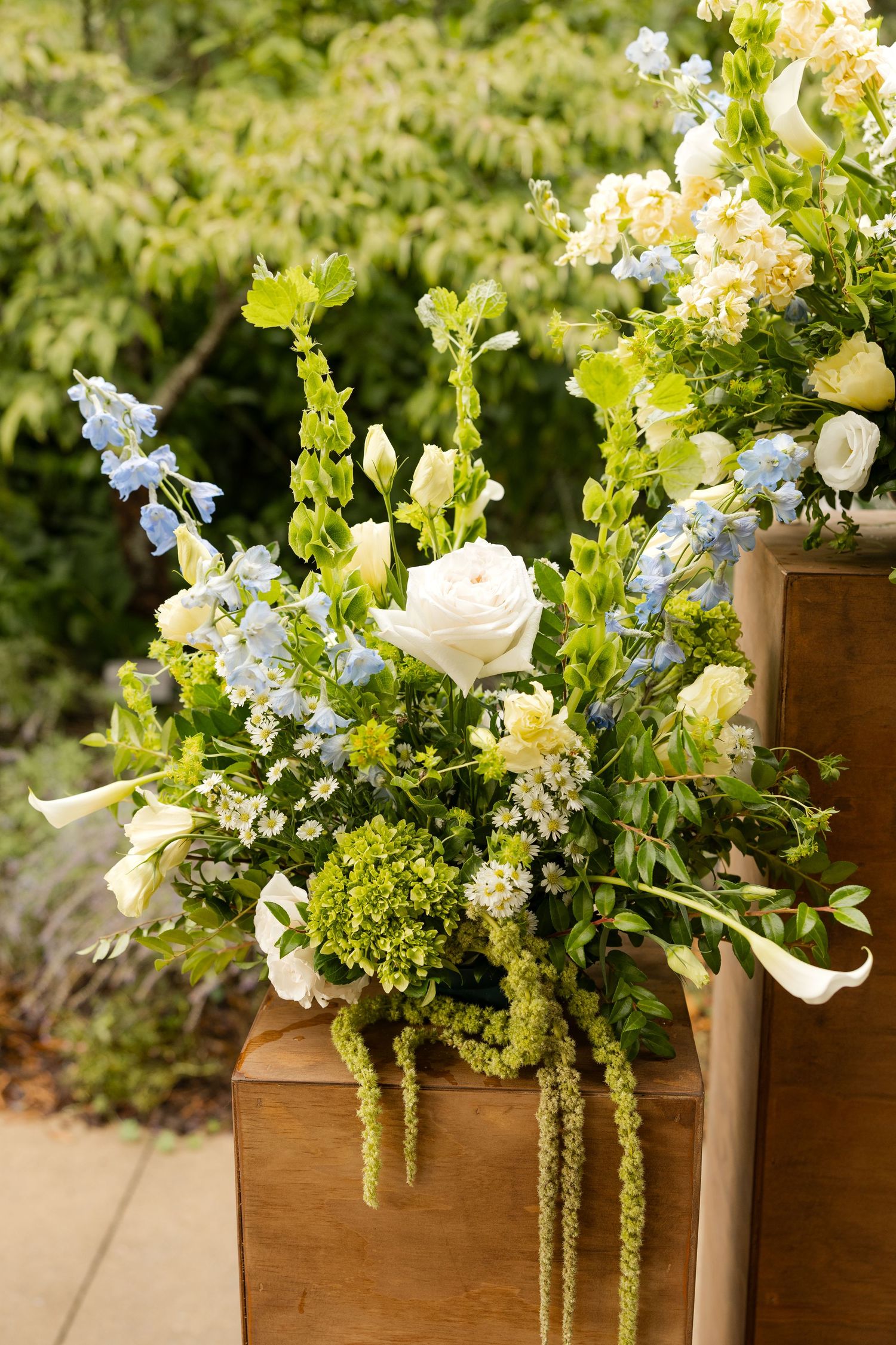 Lush floral arrangements with white roses and cascading greenery displayed on wooden pedestals.Botanical Gardens of the Ozarks