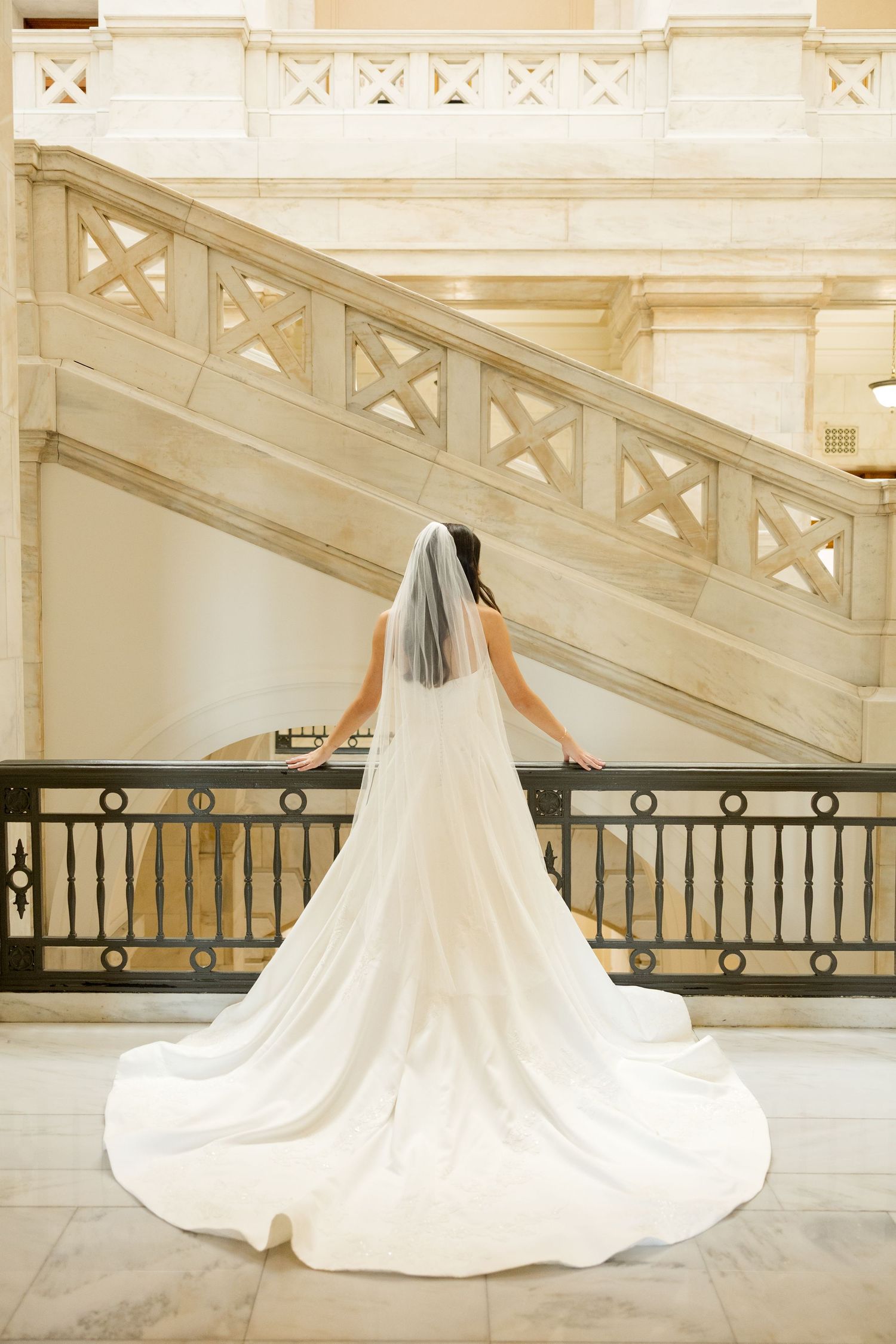 A dramatic wedding dress with a cathedral train spreads across an elegant marble hallway.