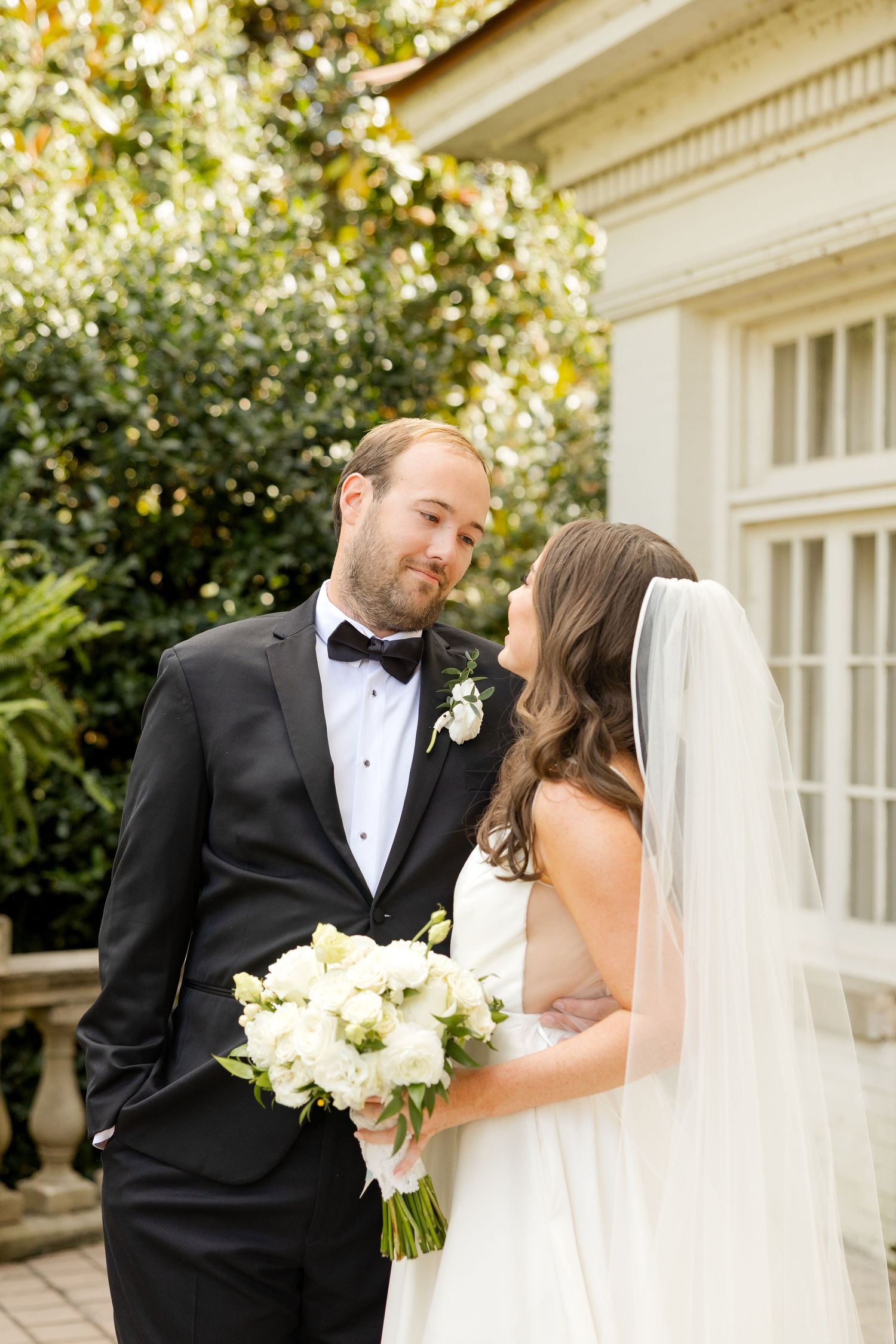 A romantic wedding couple shares tender moments on a sunny day outside an elegant white building with classic architecture.