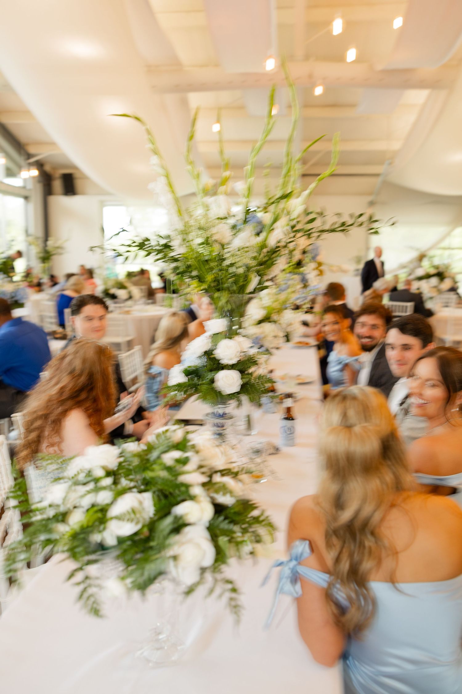 Reception venue filled with guests and elegant floral centerpieces in white and green.Cold Springs Events.