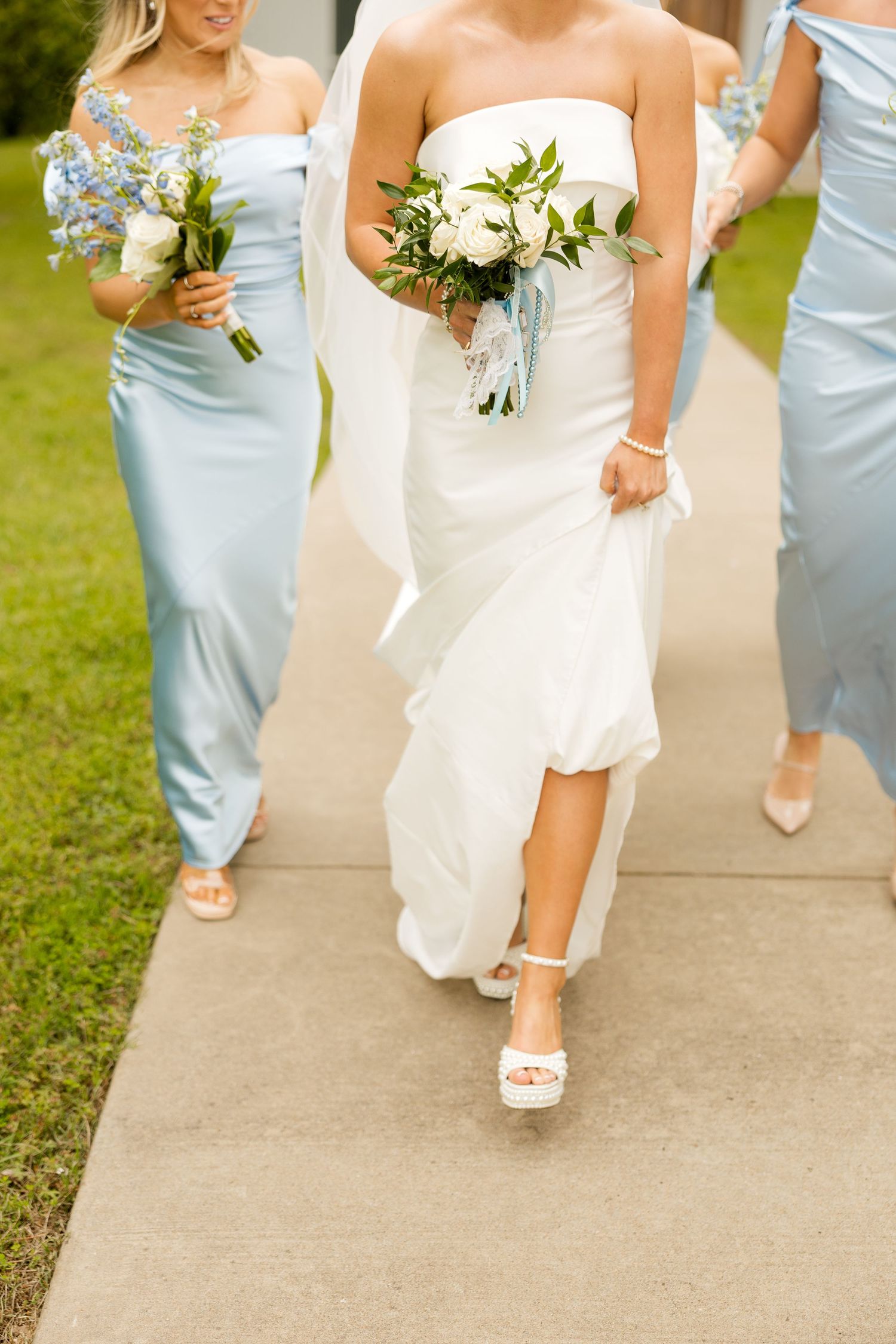 Wedding party members walking in light blue dresses and white gowns showing their shoes on concrete path.Cold Springs Events