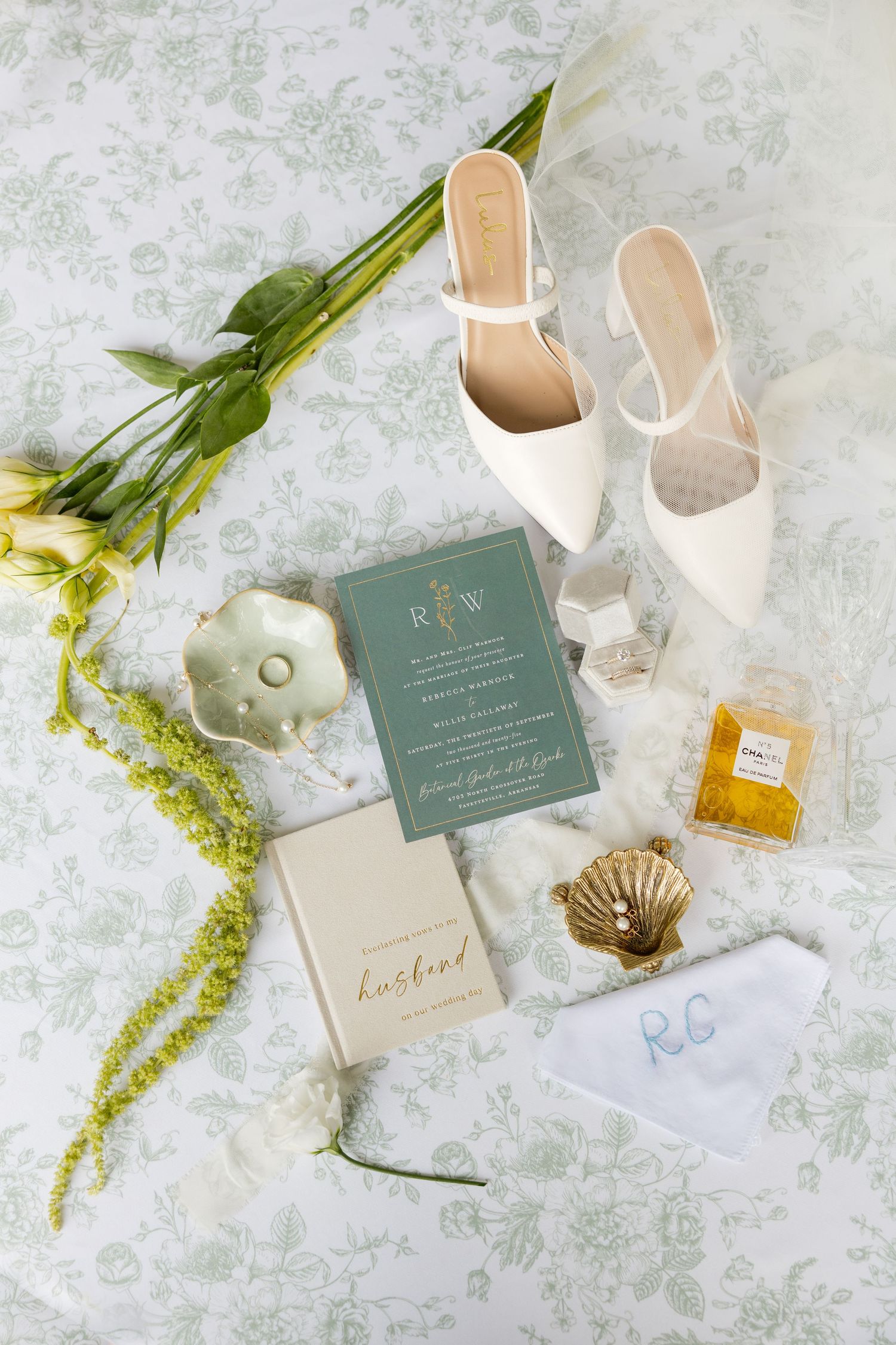 Wedding details flat lay with invitations, white shoes, and perfume on a textured background.Botanical Gardens of the Ozarks