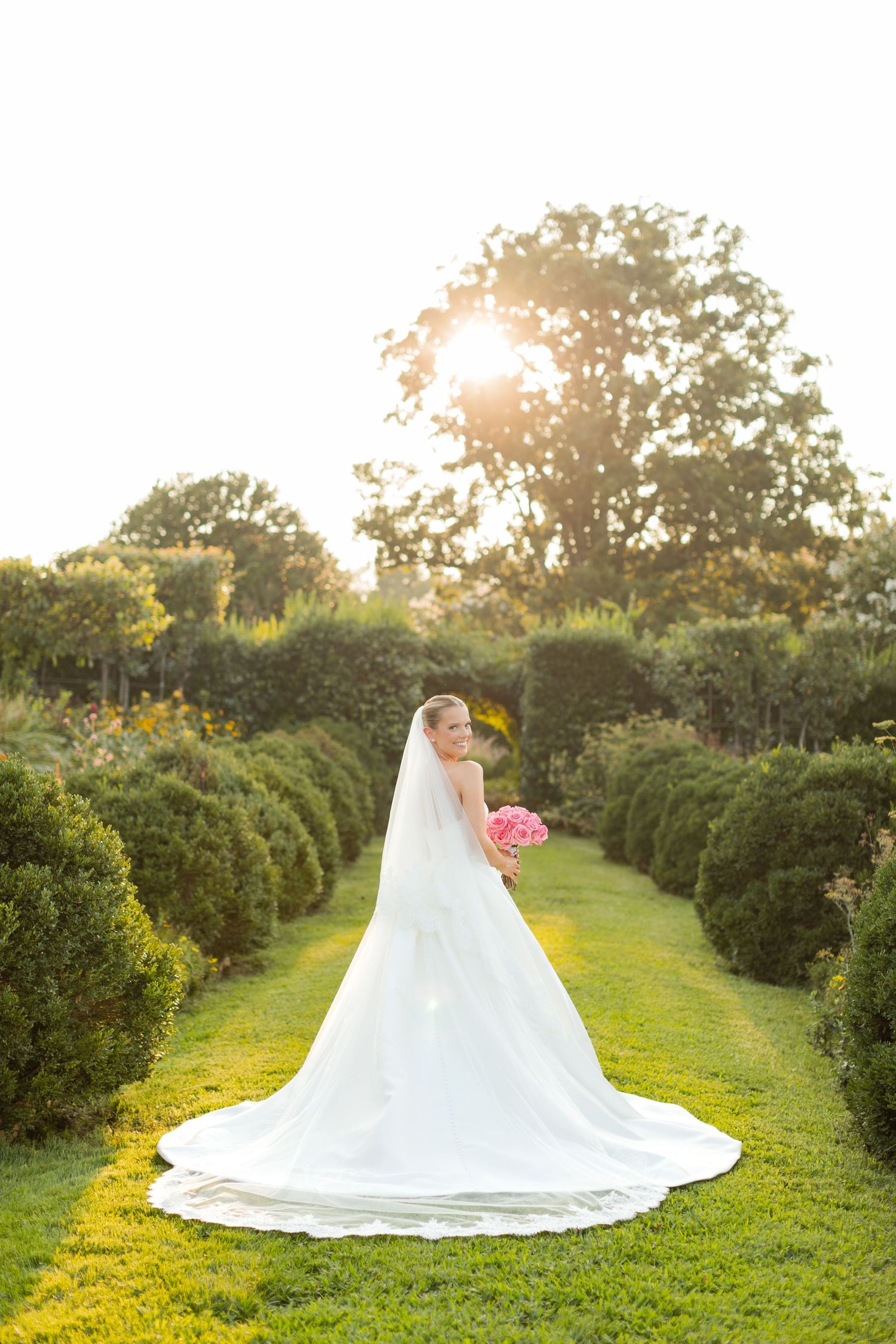 White wedding dress with dramatic train photographed in a garden setting during golden hour.