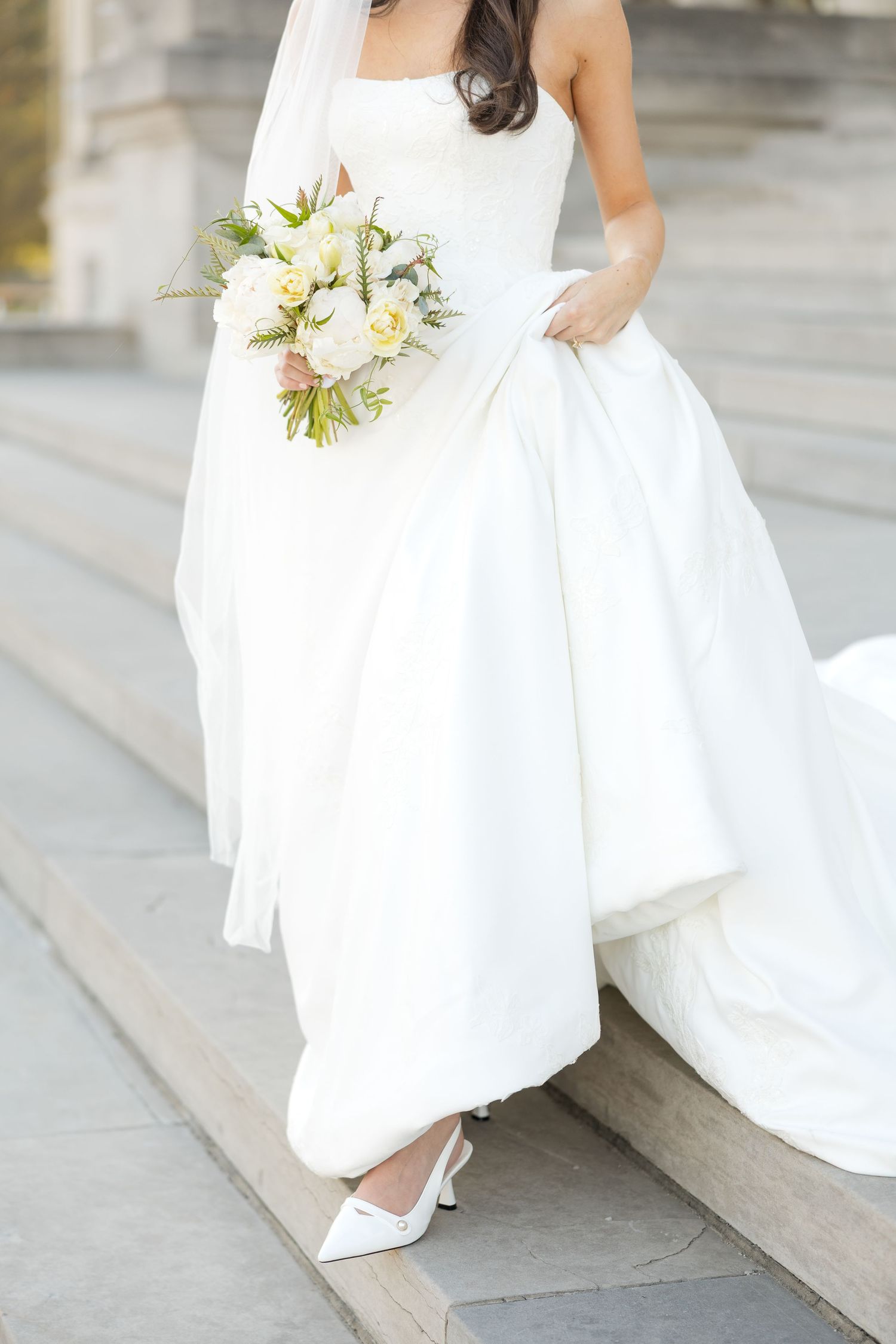 Elegant bridal details showing white dress and bouquet against stone architecture.