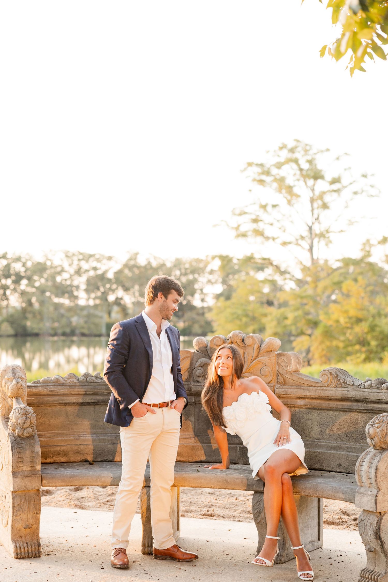 A couple shares a romantic moment at sunset in a rustic outdoor setting with wooden barrels and autumn foliage.
