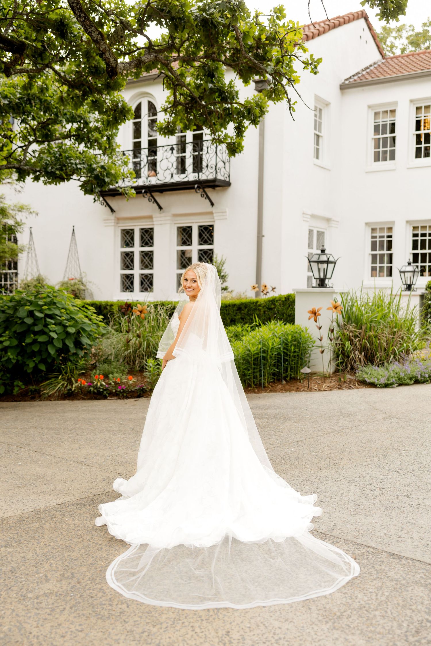 A flowing white wedding gown with a long train photographed in sequence against a classic white mansion exterior.
