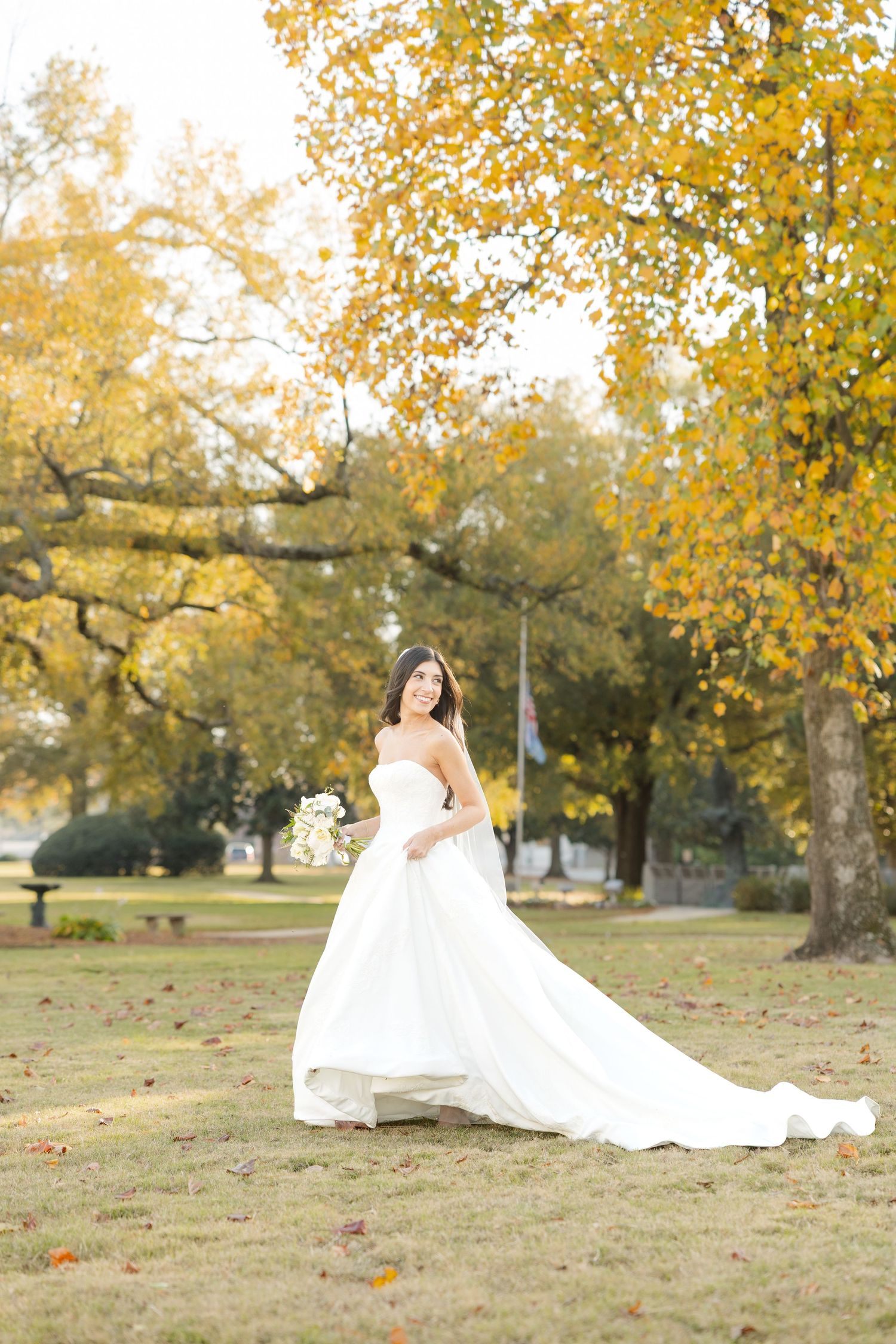 Wedding dress flowing across autumn grass with golden trees in background.