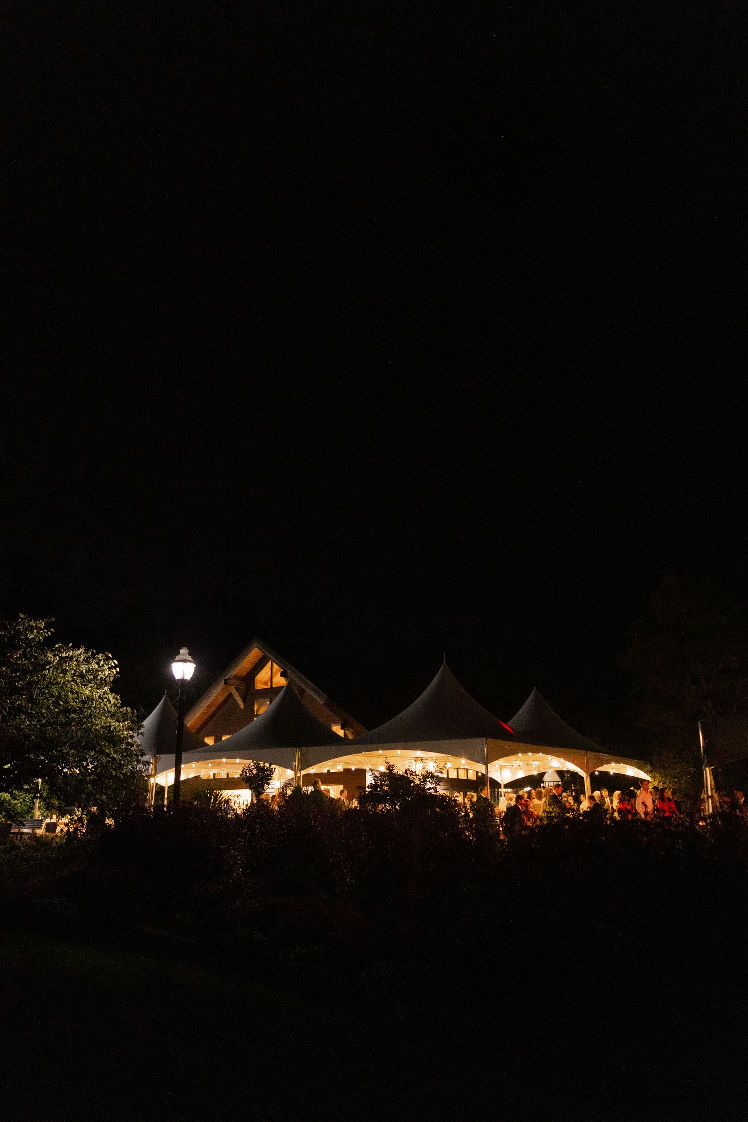 Illuminated wedding tent glowing at night with string lights and gathered guests.Botanical Gardens of the Ozarks