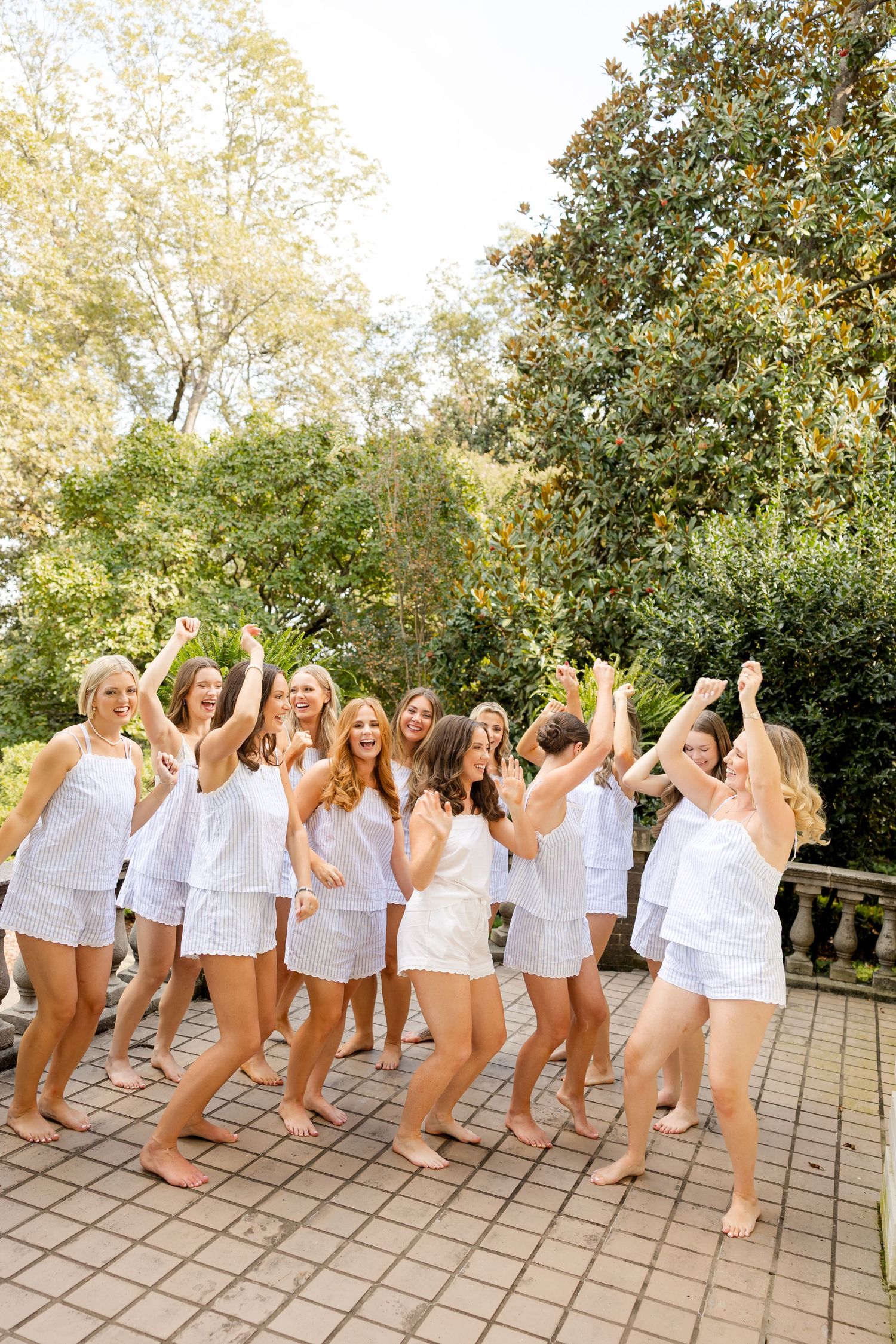Group wearing matching white outfits dance and celebrate on an outdoor stone patio.