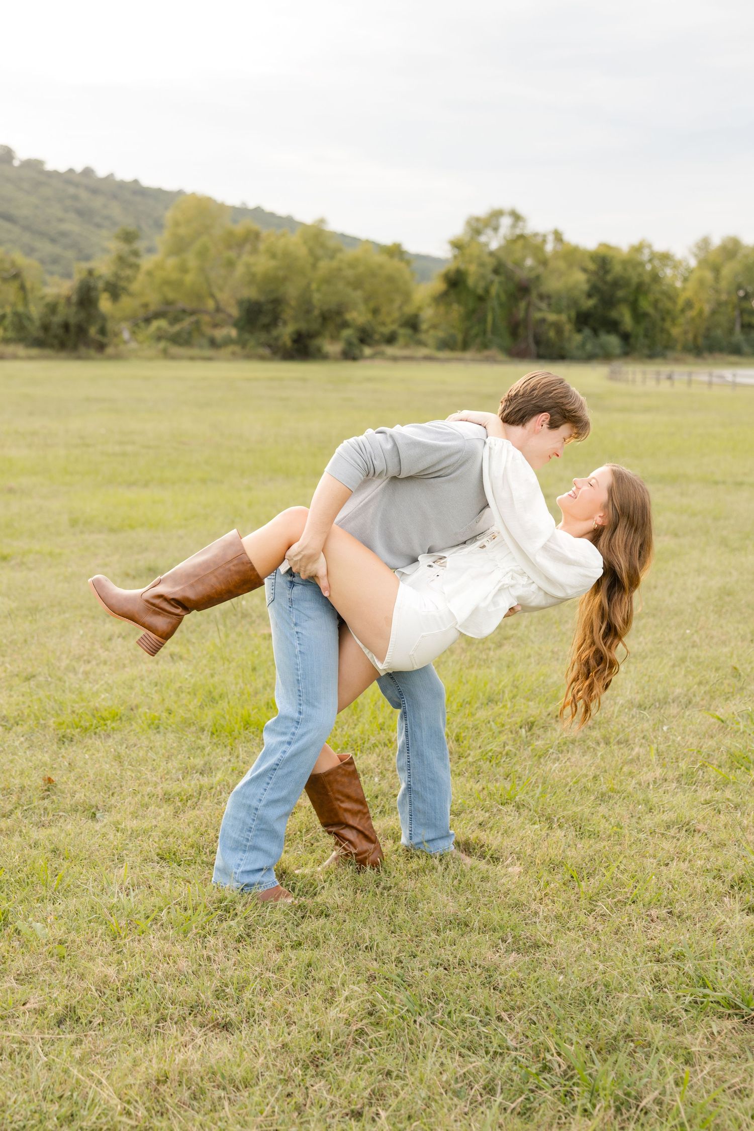 Playful couple performs a dramatic dip pose in a grassy field on a bright autumn day.