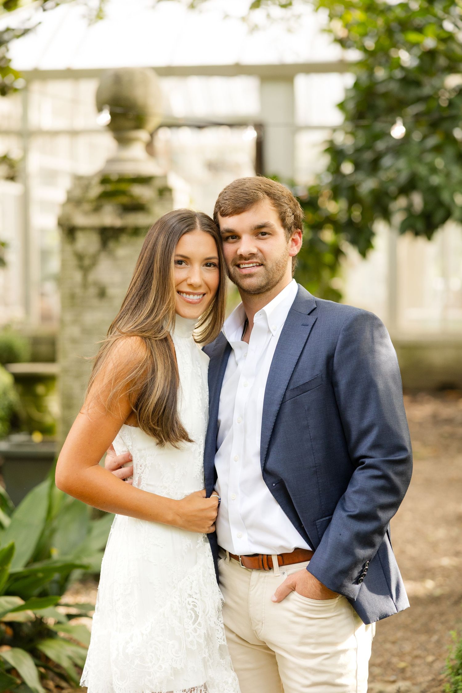 A romantic couple poses together in a garden setting wearing white and navy blue outfits.