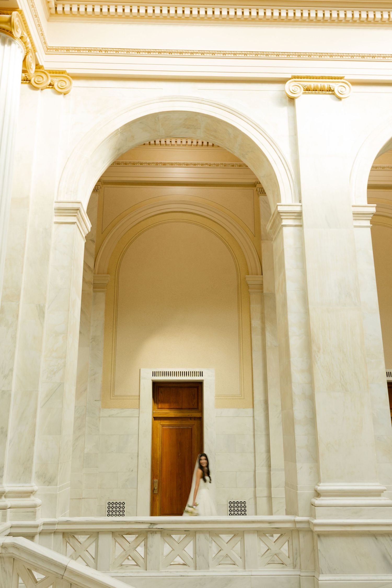 An elegant white marble hallway with classical columns and arches features a wooden door at the end.