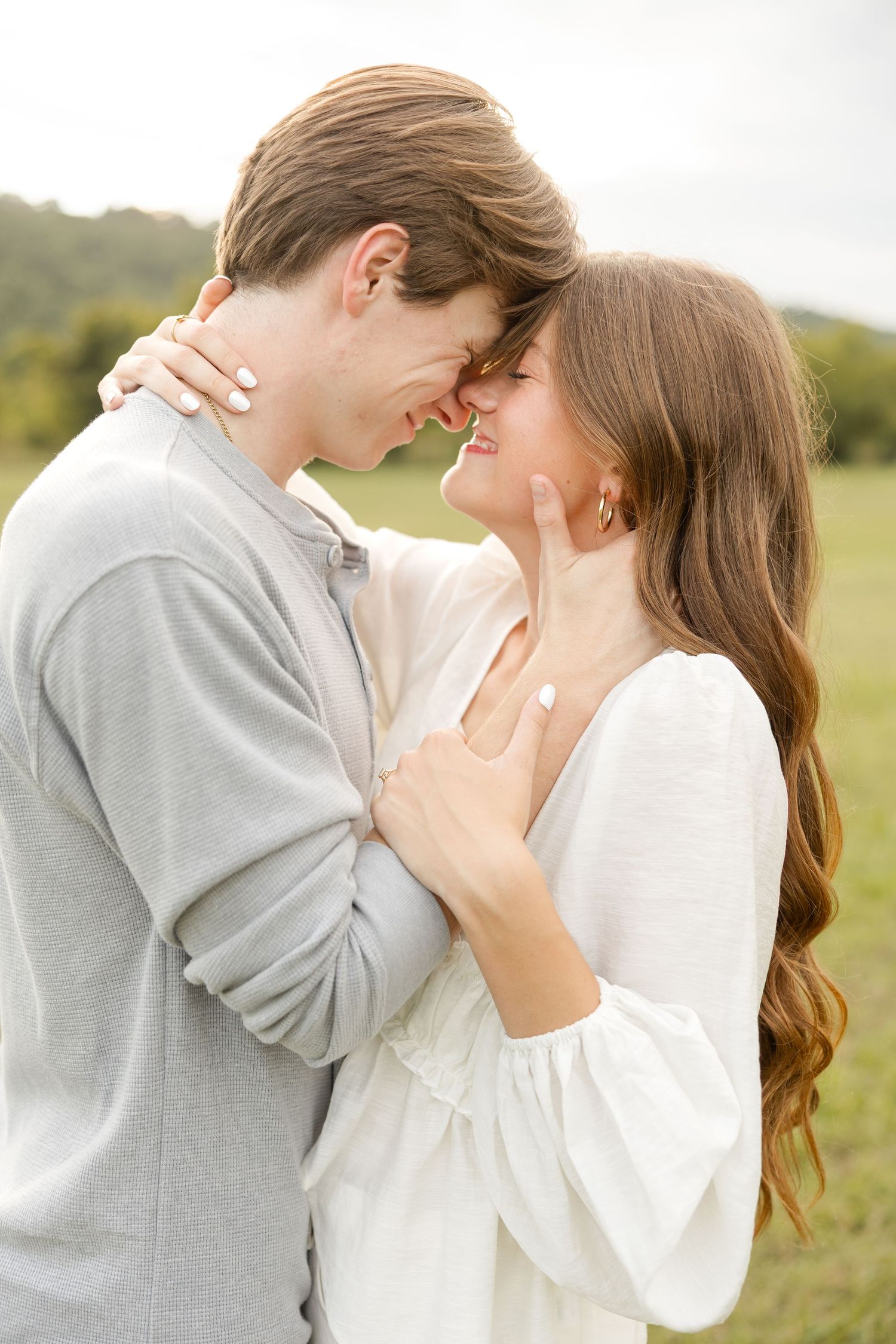 A romantic couple embraces in a sunny field wearing gray and white casual clothing.
