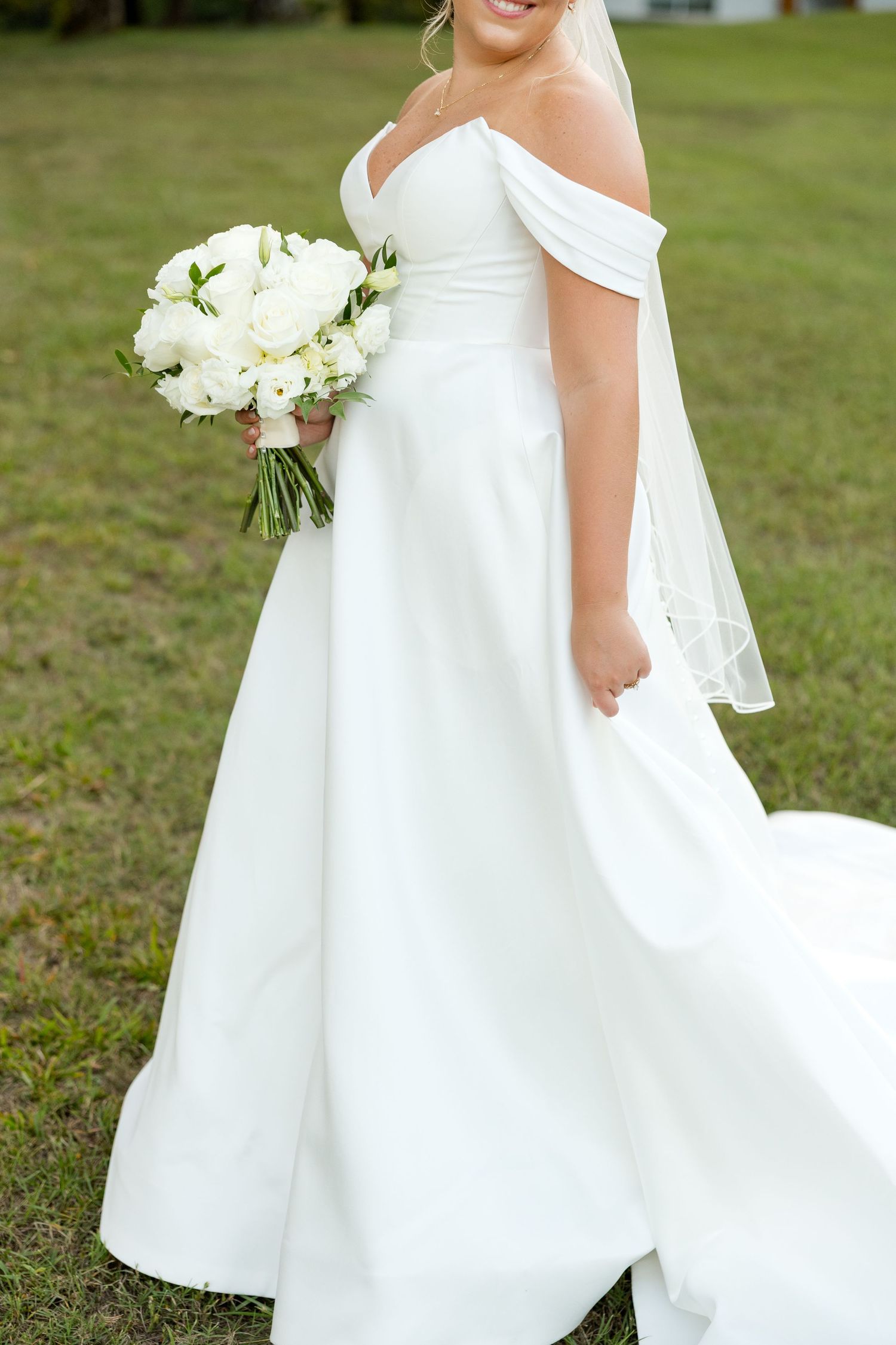A flowing white wedding dress with cap sleeves and bouquet photographed on a grassy lawn.