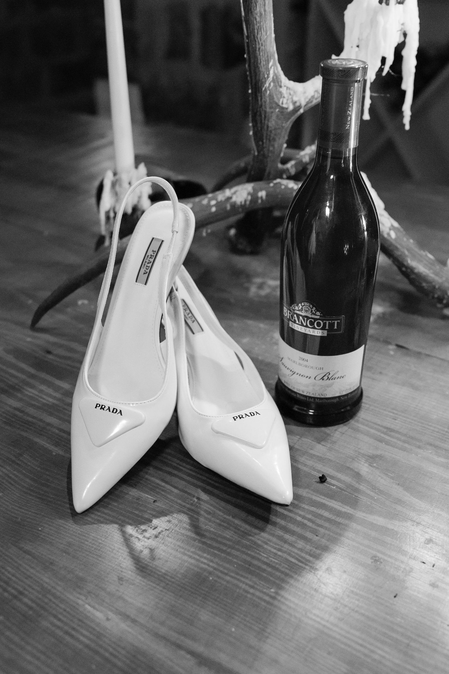 A series of black and white photos showing white high heeled shoes next to wine bottles on a wooden surface. Goodwin Manor.