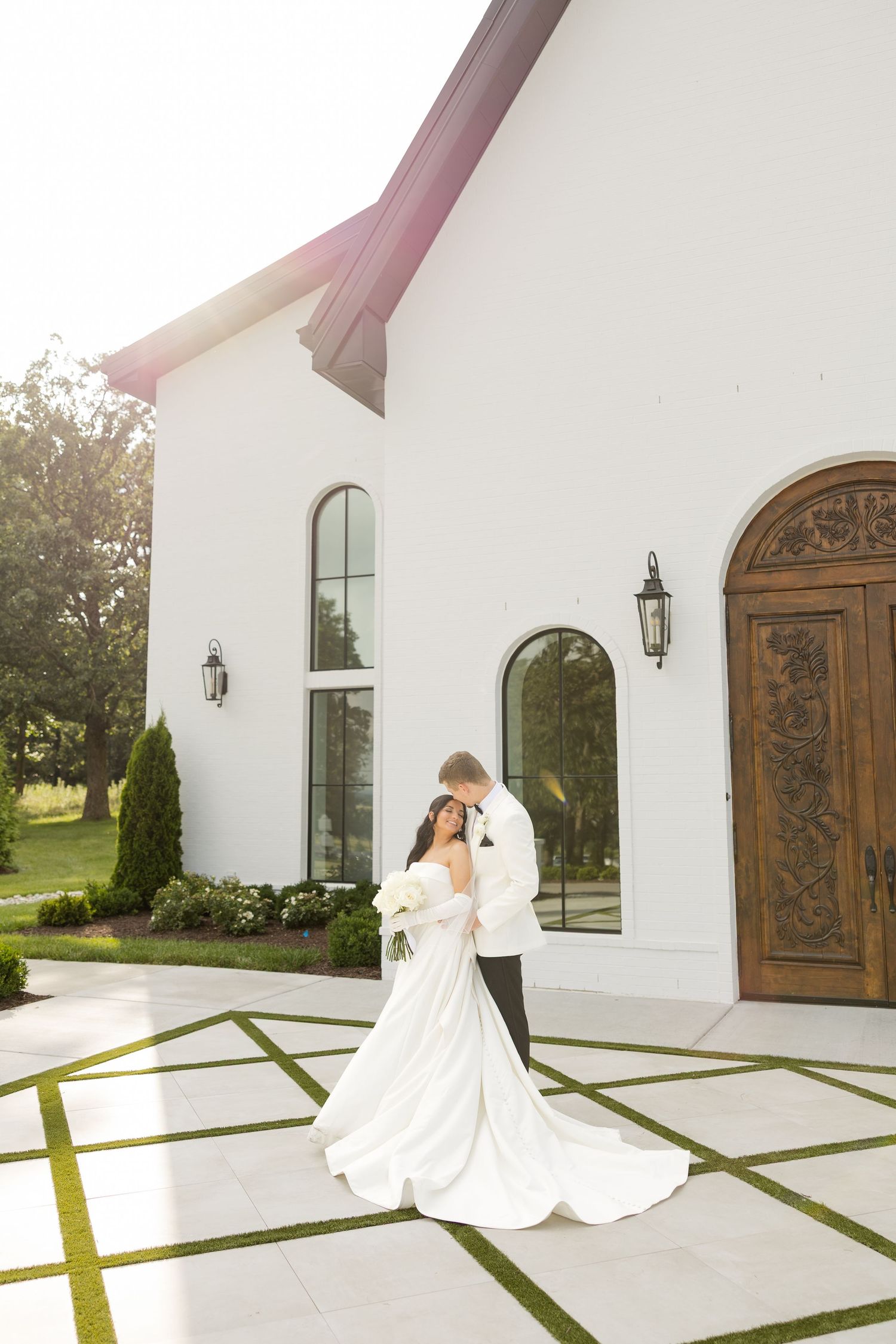 Bride and groom dance outside a white chapel with ornate wooden doors and landscaping. Grand at the Springs.