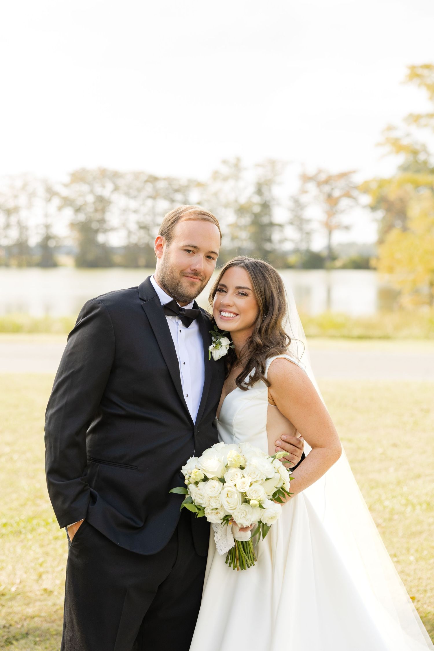 Newlyweds pose together outdoors holding white bouquet in formal wedding attire.Marlgsate Plantation