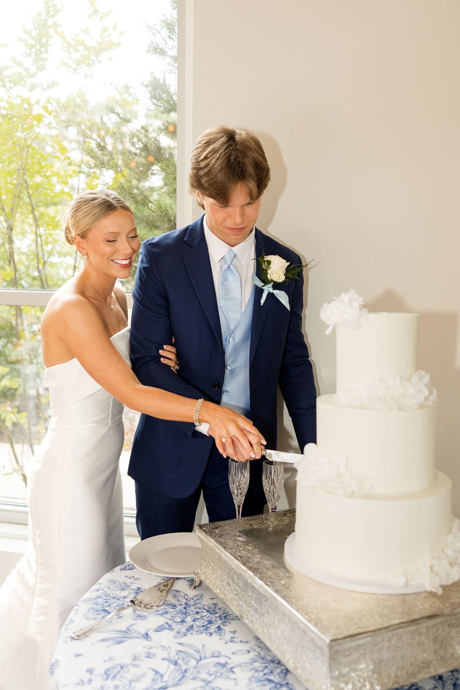 A couple cuts into their elegant white wedding cake together during their reception.Cold Springs Events.