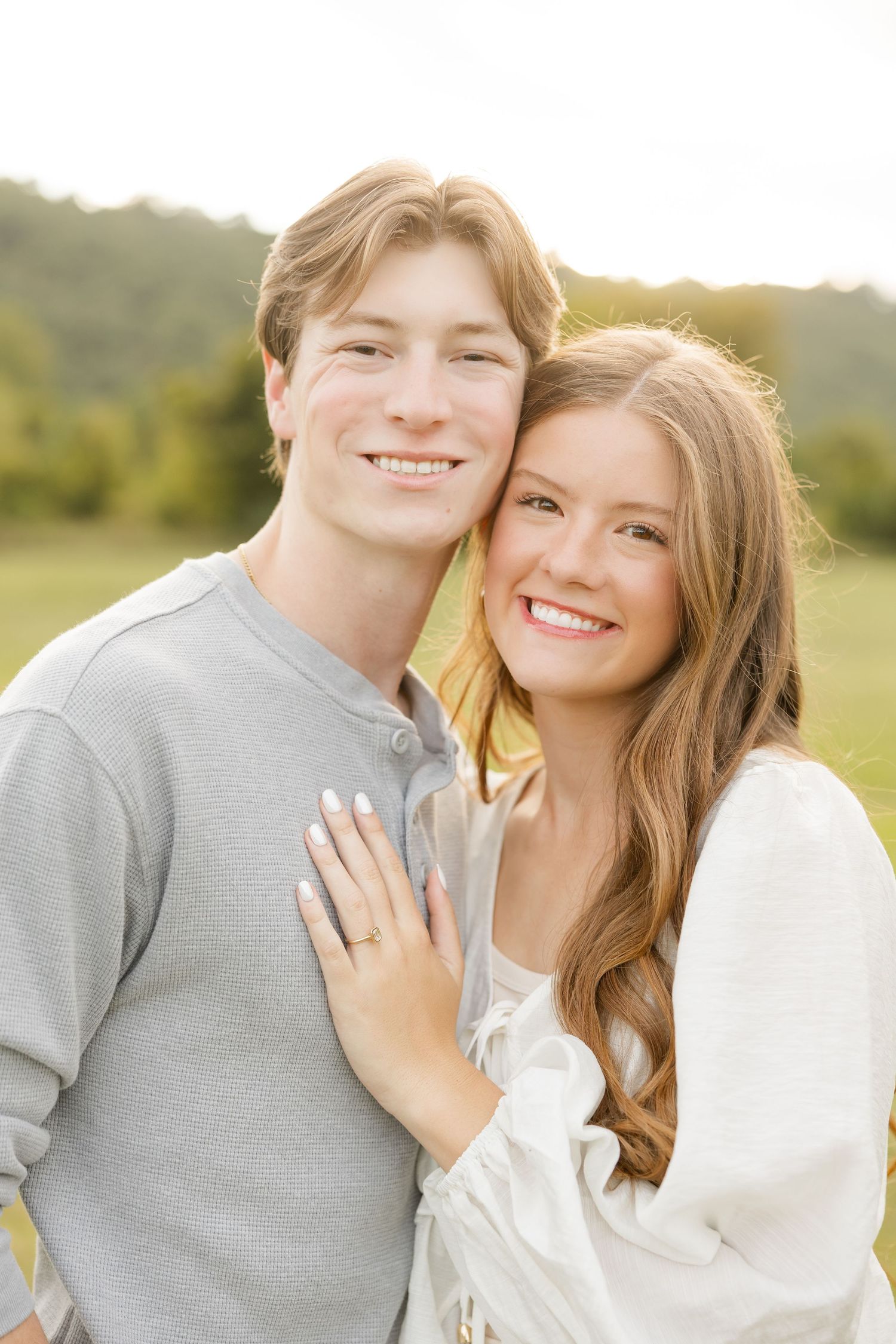 A happy couple poses closely together outdoors in a natural setting during golden hour.
