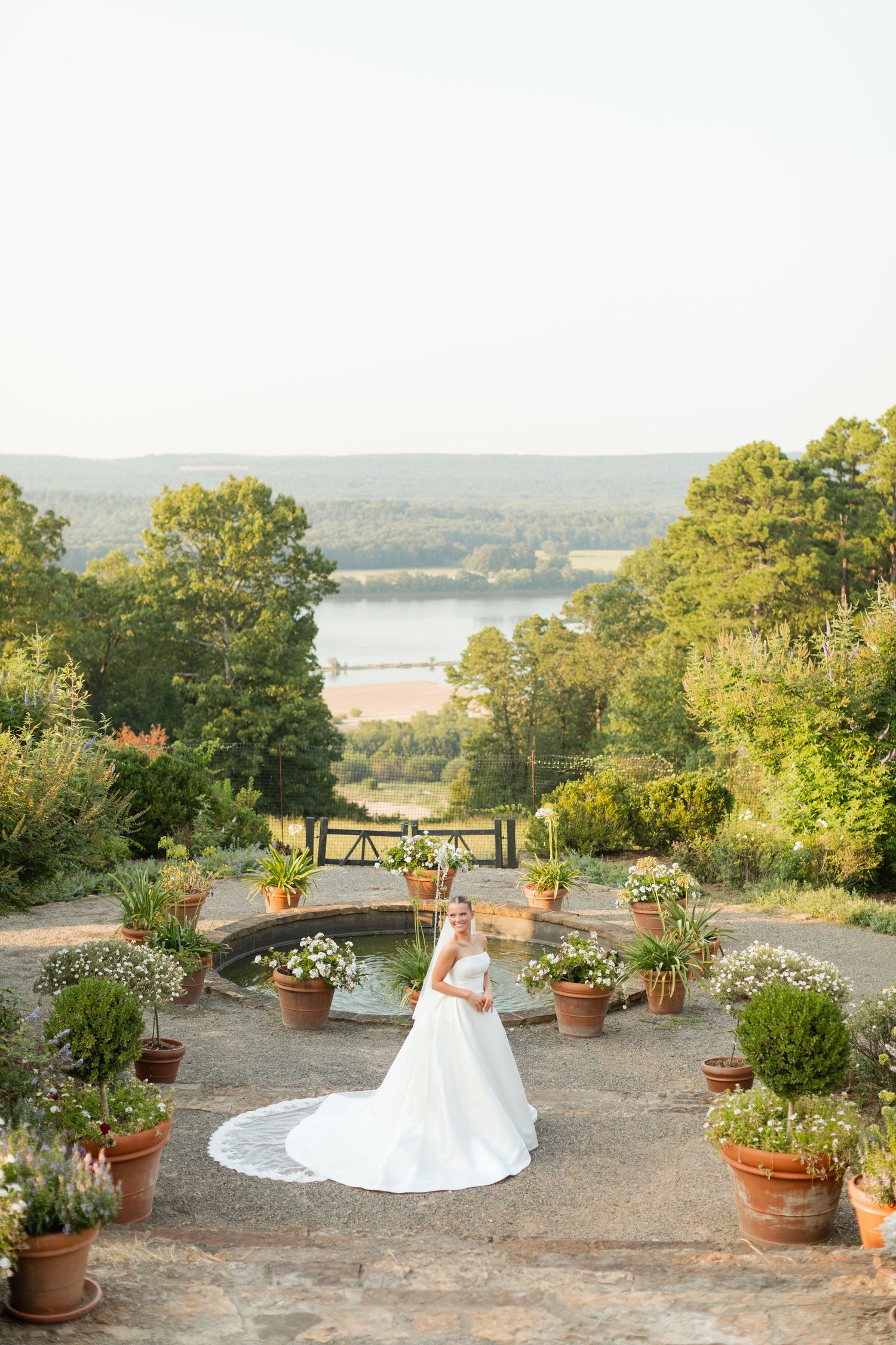 A scenic garden terrace overlooks a serene lake, decorated with potted plants and flowers for an outdoor wedding ceremony.