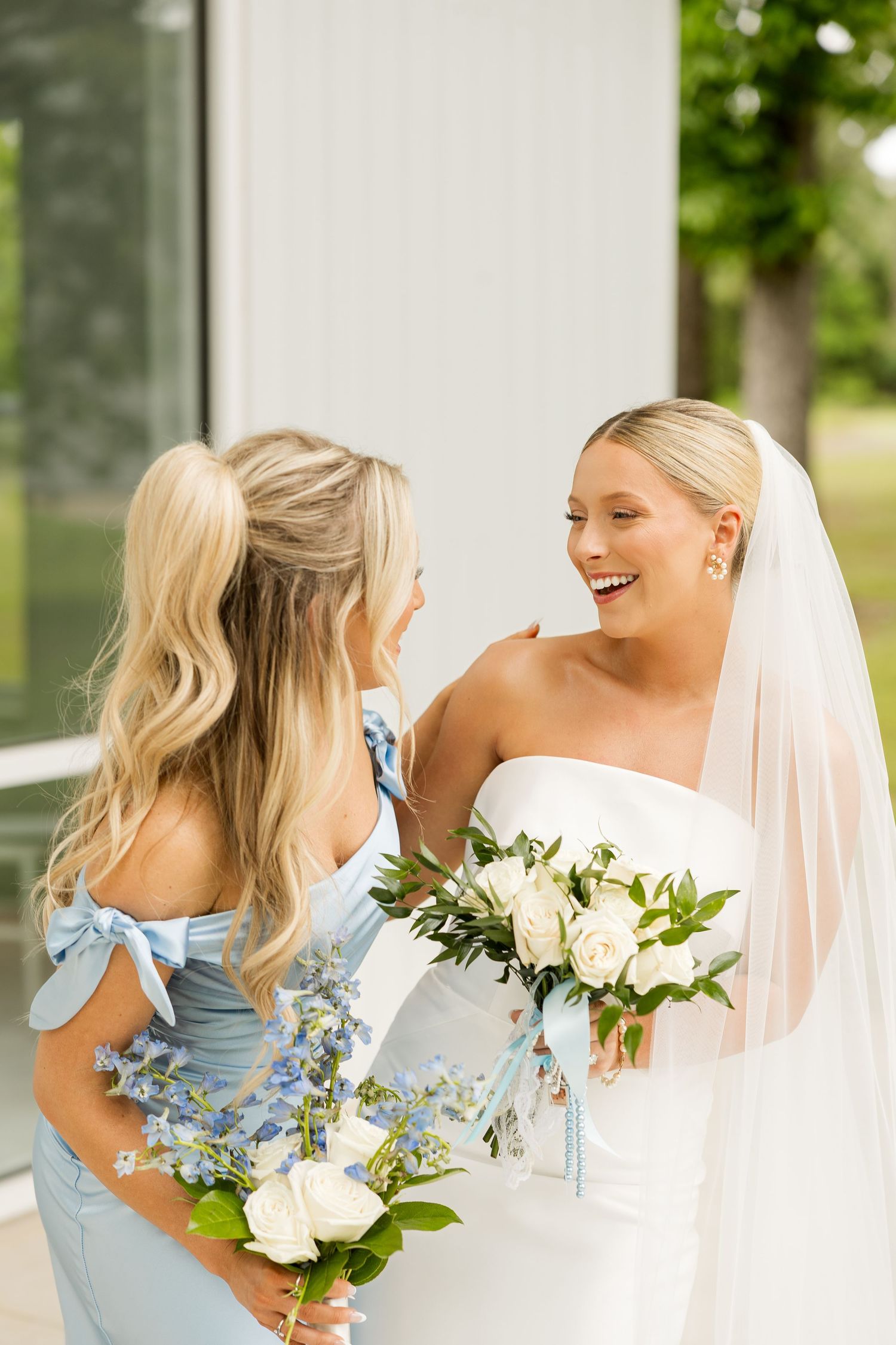 A bride in white shares a joyful moment with her bridesmaid wearing a light blue dress.Cold Springs Events