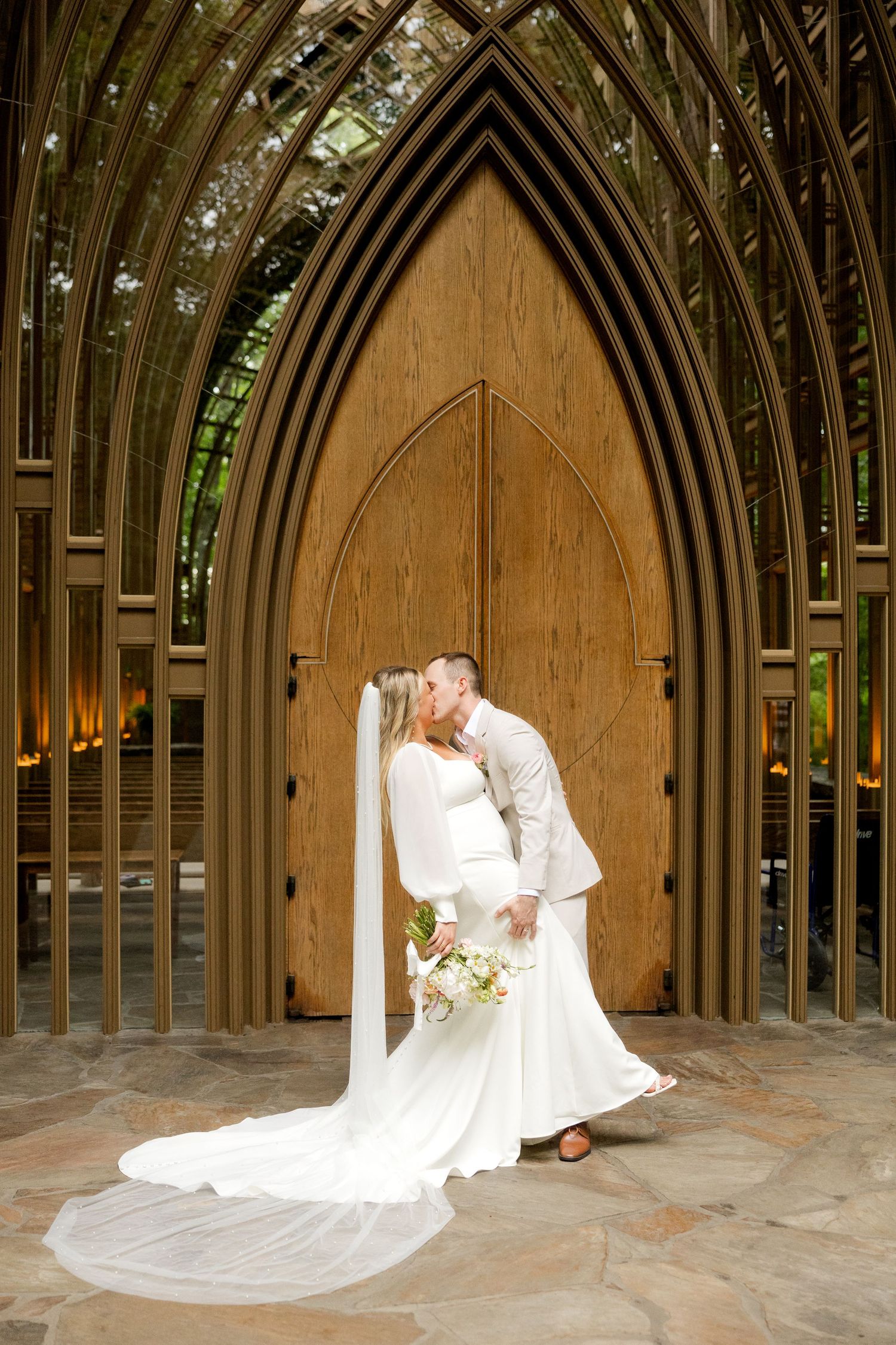 A romantic wedding photo in front of a wooden Gothic arch door with a flowing white veil and elegant dress.Mildred B. Cooper Chapel
