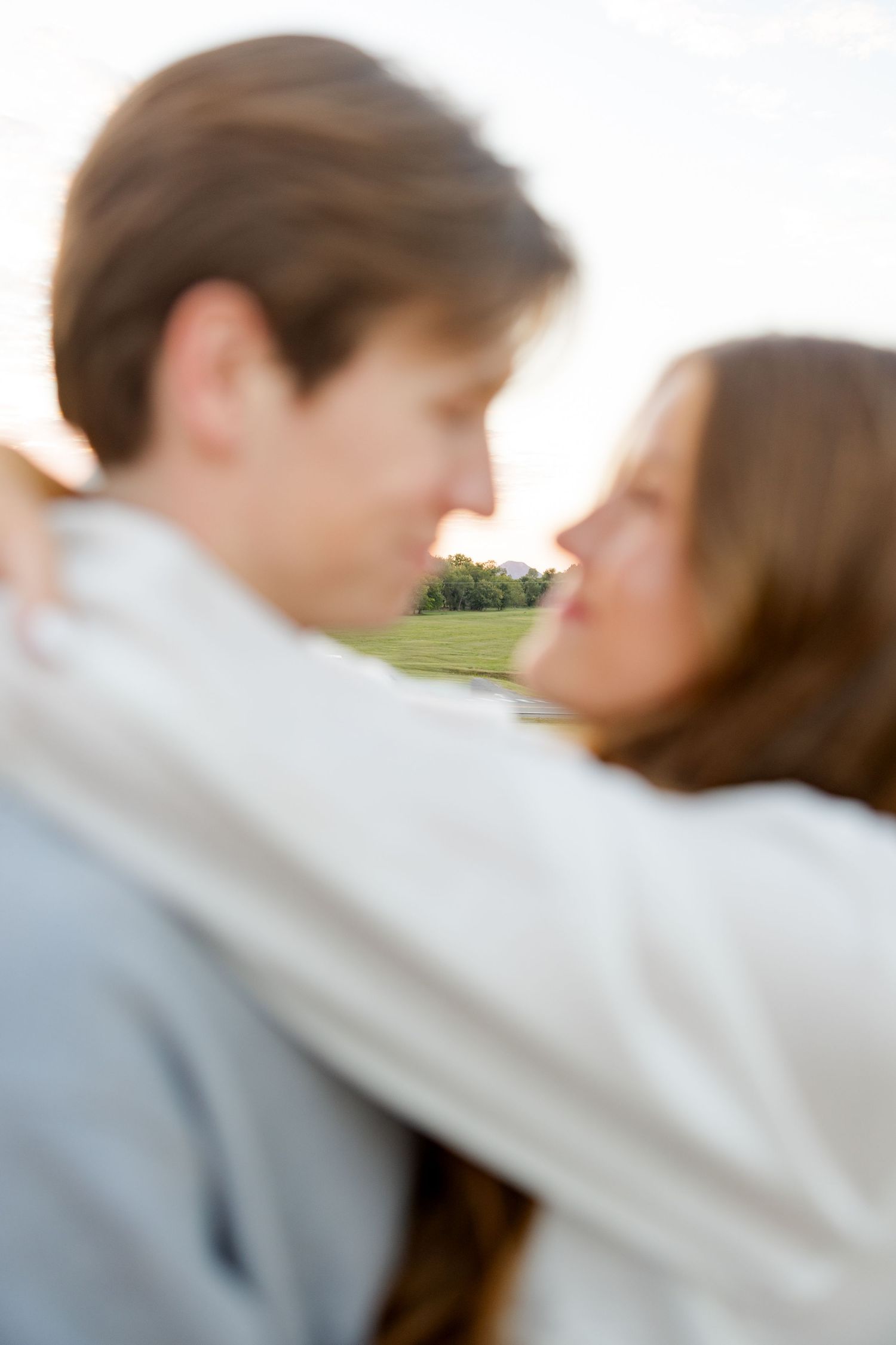 A romantic couple sharing a tender moment in a soft focus outdoor setting during sunset.