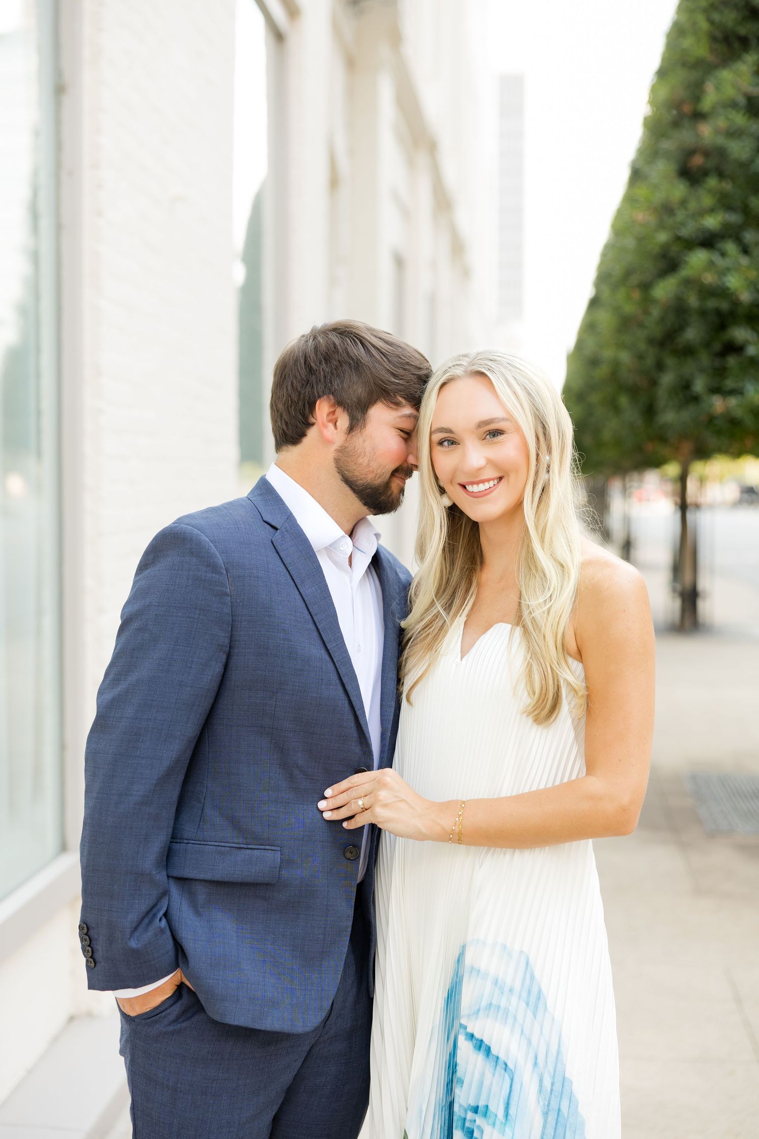 A couple shares romantic moments in a white outdoor colonnade setting wearing navy and white attire.