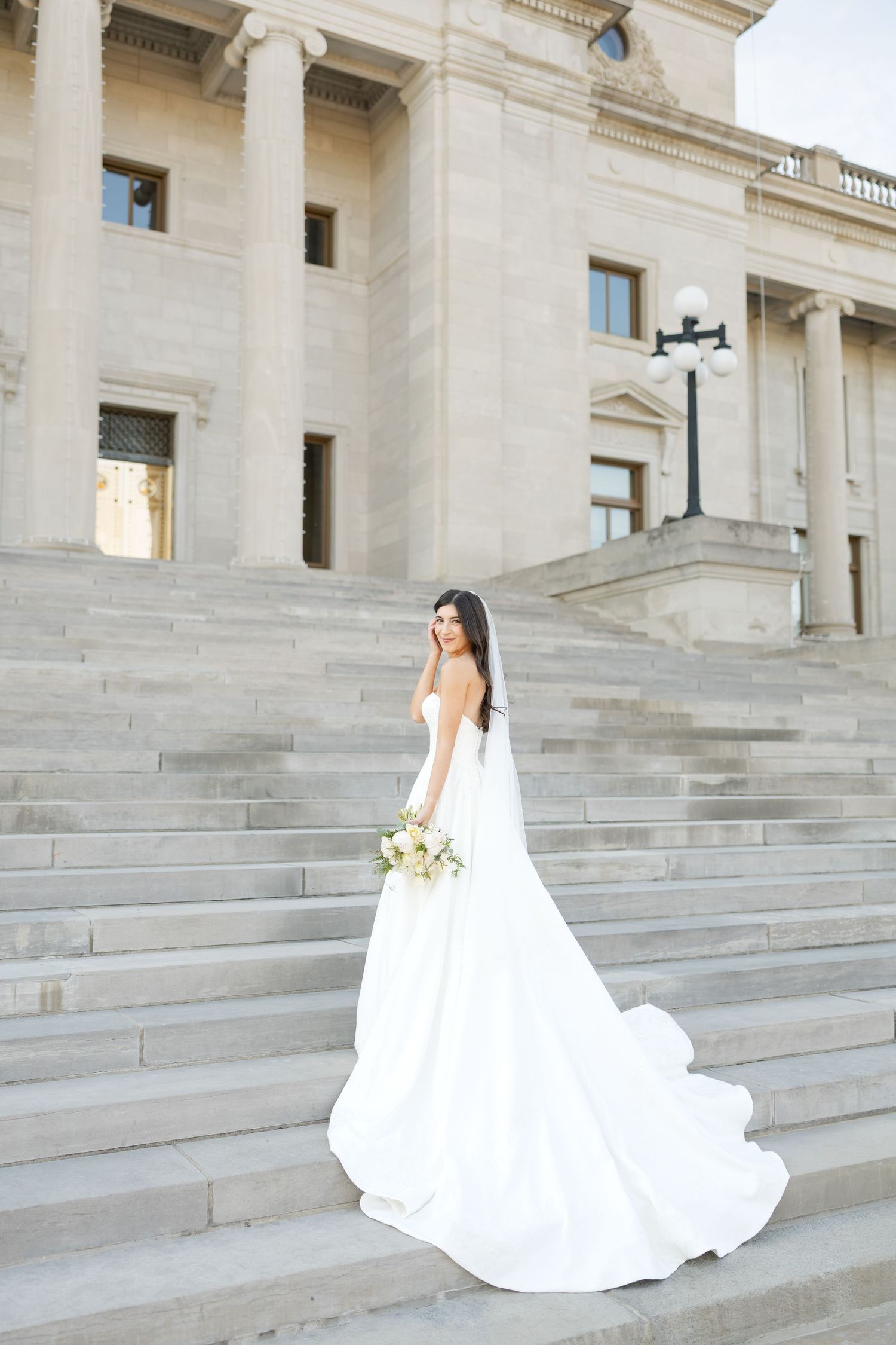 A stunning white wedding gown photographed on the steps of a majestic stone building with columns.