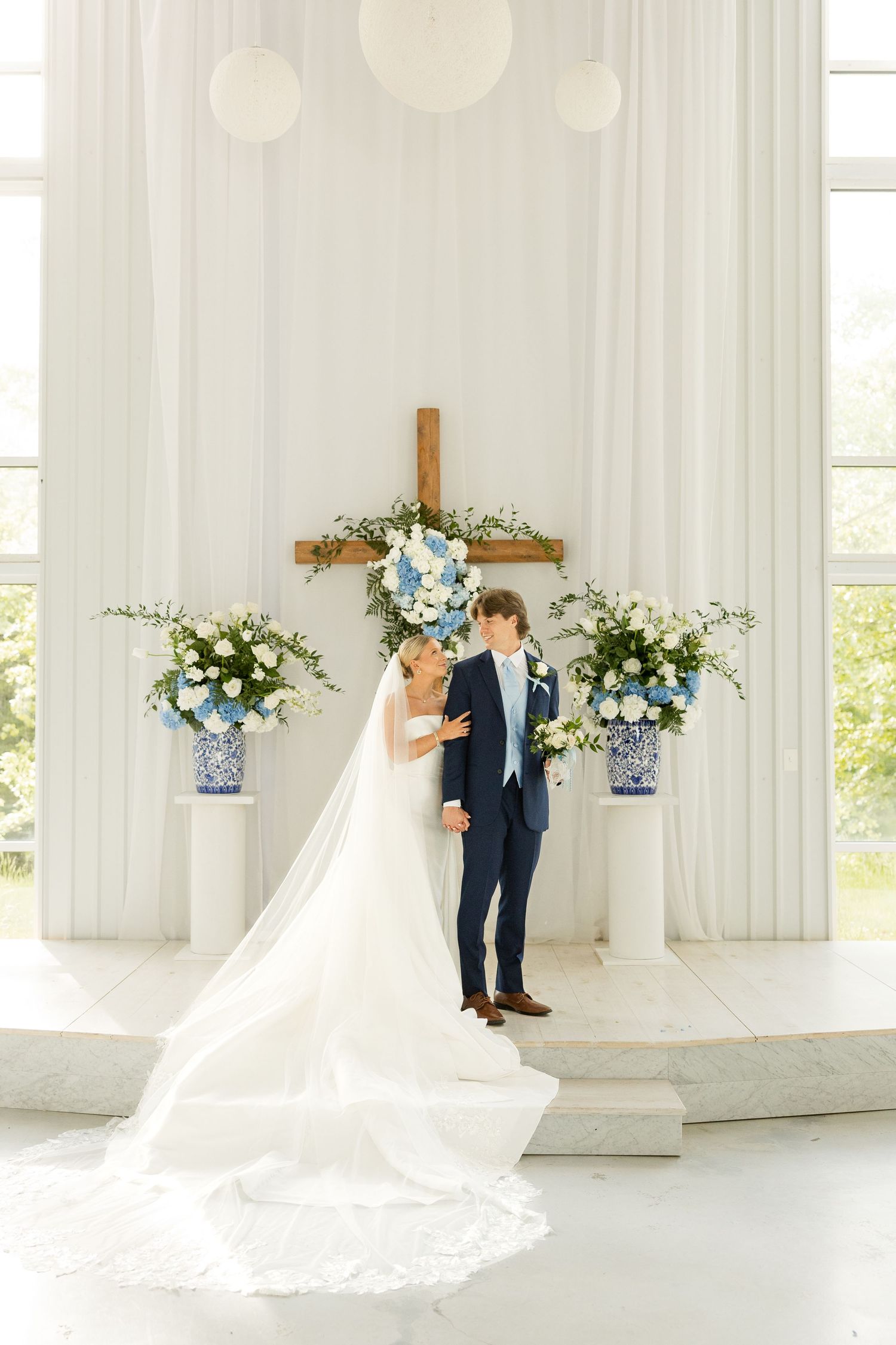 Wedding couple posing in bright white chapel with dramatic train of wedding dress visible.Cold Springs Events