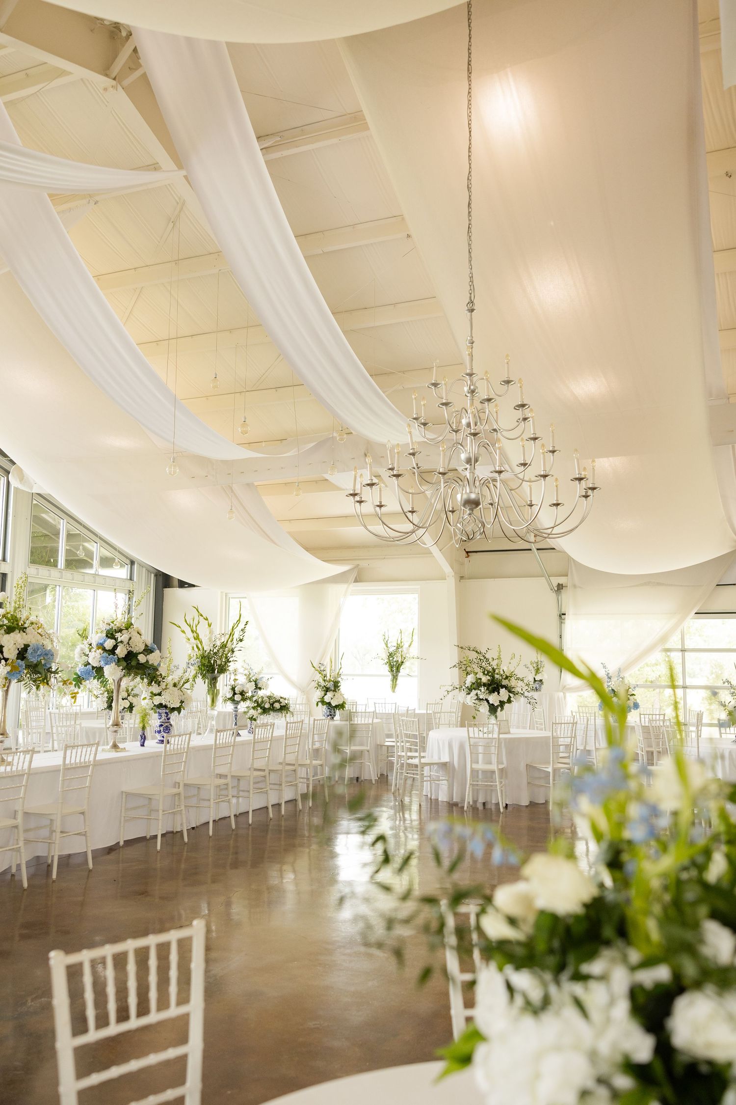 Elegant white wedding reception venue with draped ceilings, chandeliers and white chiavari chairs.Cold Springs Events.