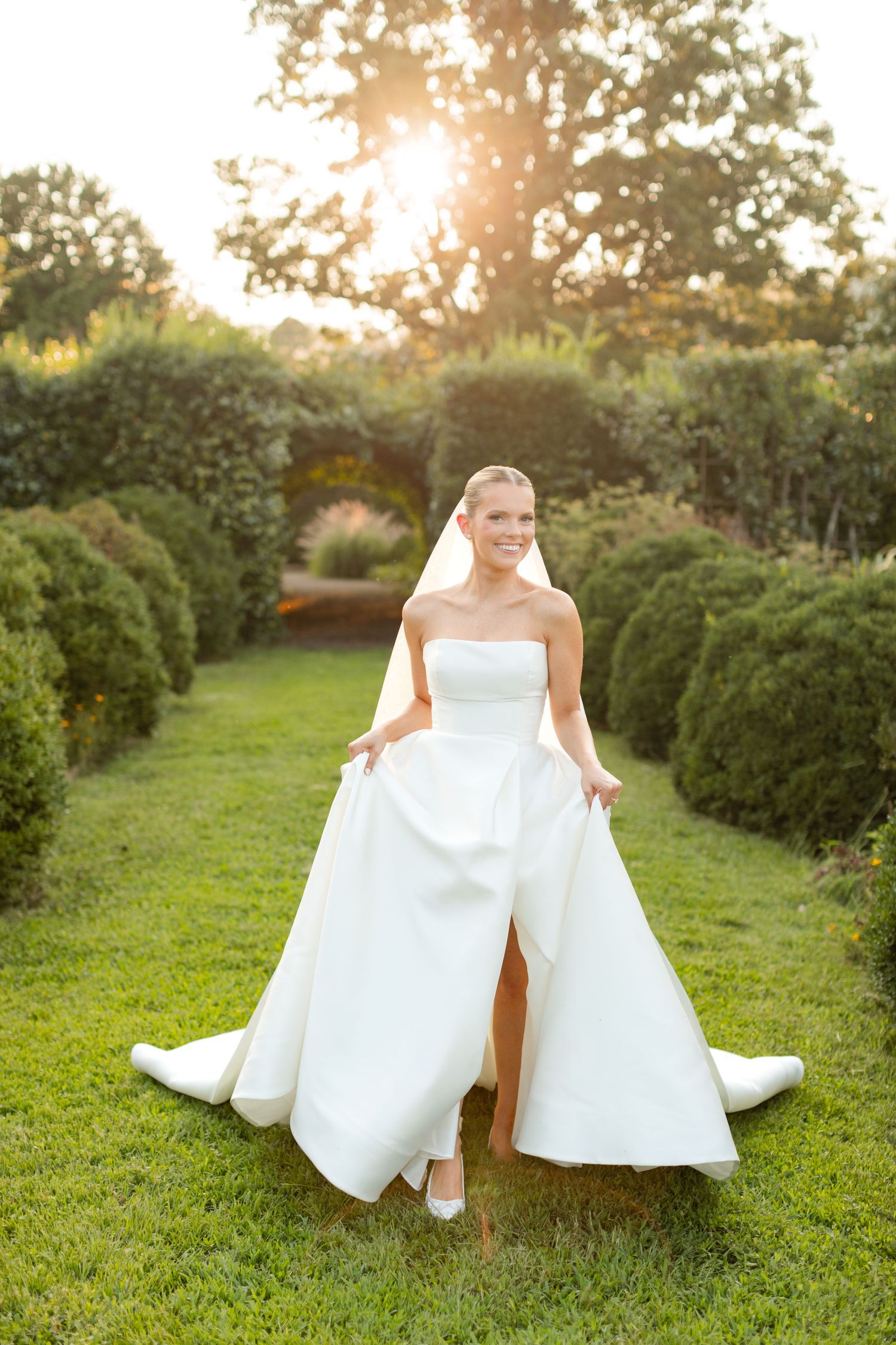 A white wedding gown spreads elegantly across vibrant grass in a garden setting.