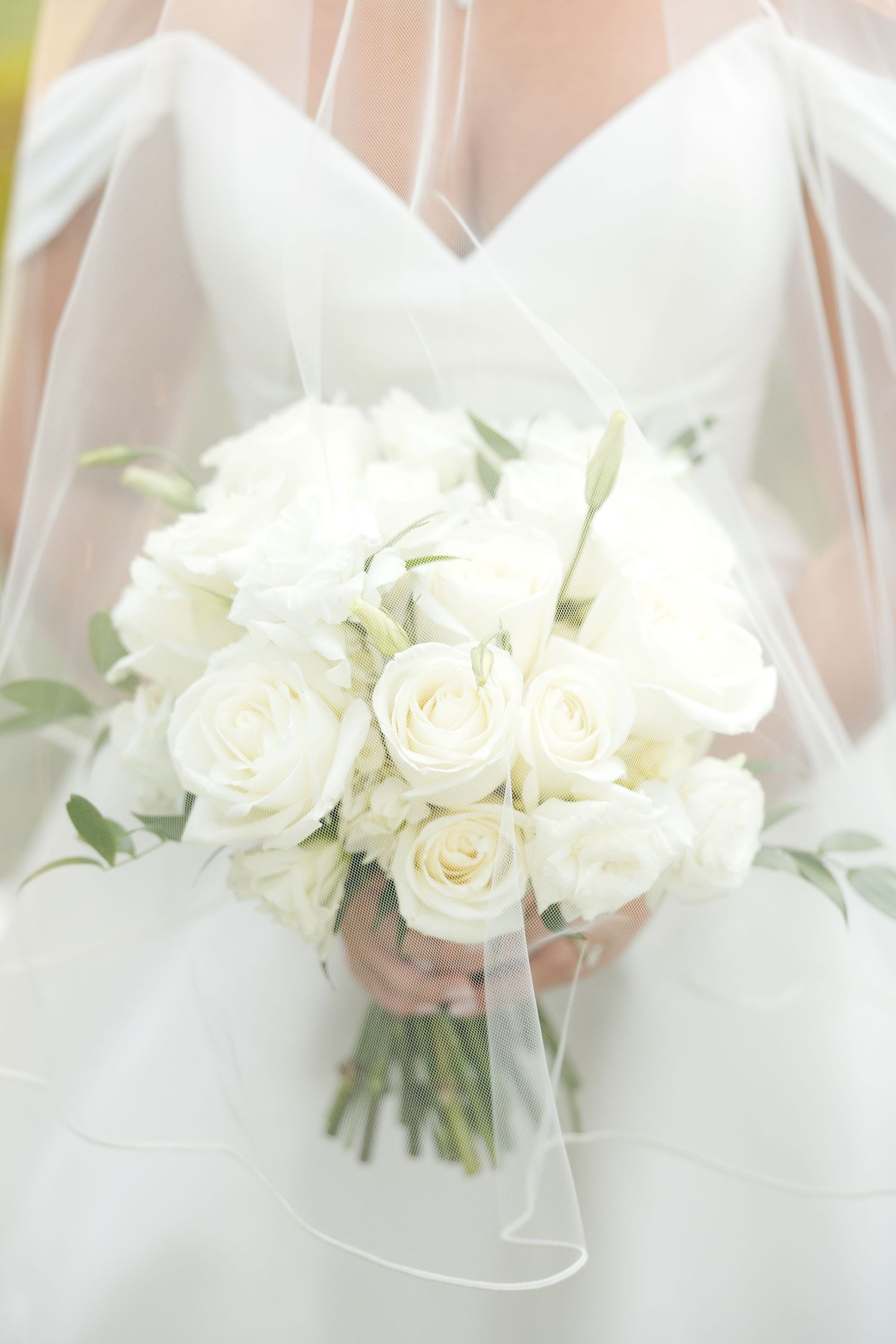 Elegant white rose wedding bouquets held by bridesmaids in matching white dresses at an elegant ceremony.