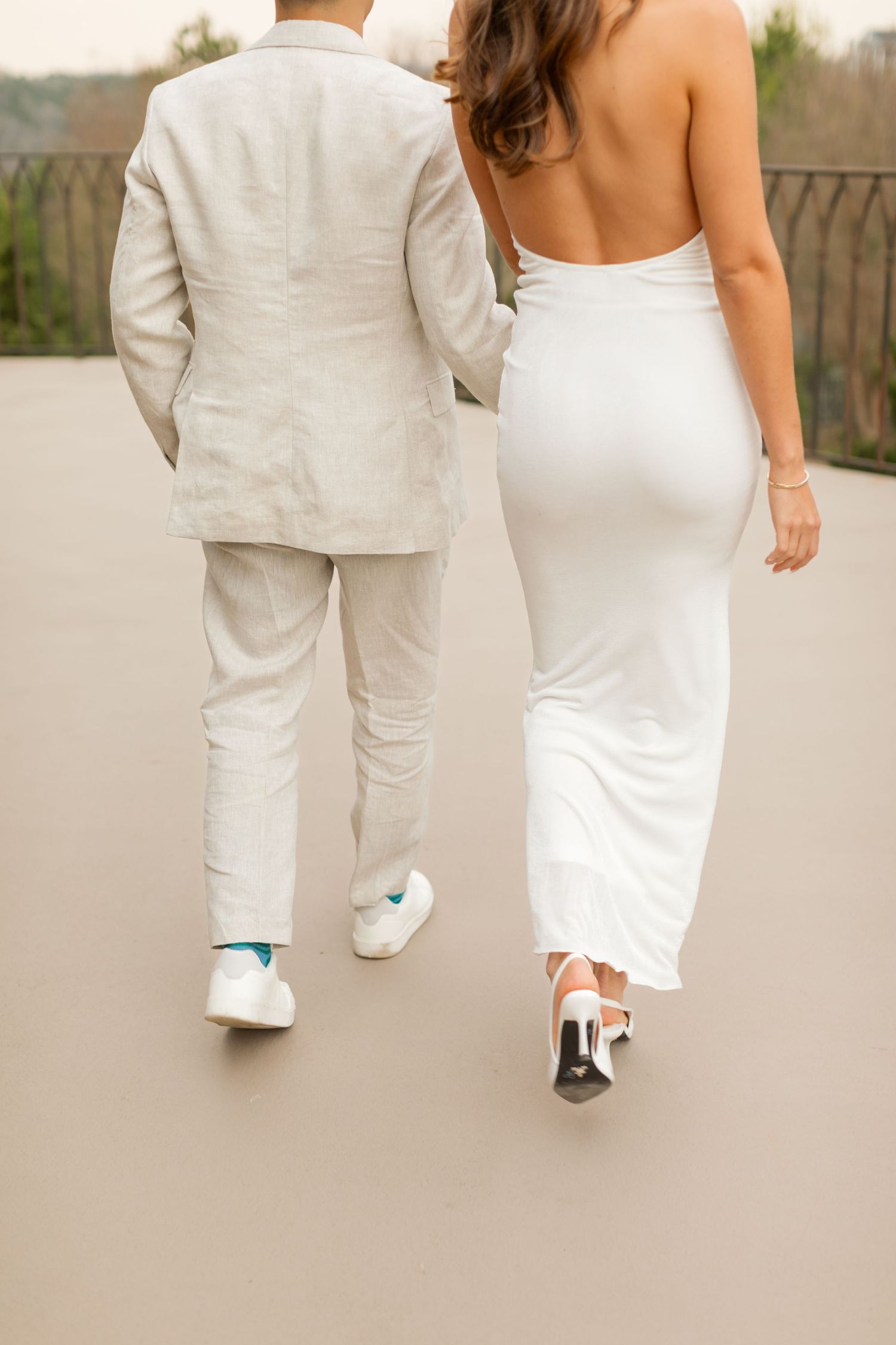Two people in white formal attire walk together on a light colored surface, photographed from behind. Goodwin Manor.