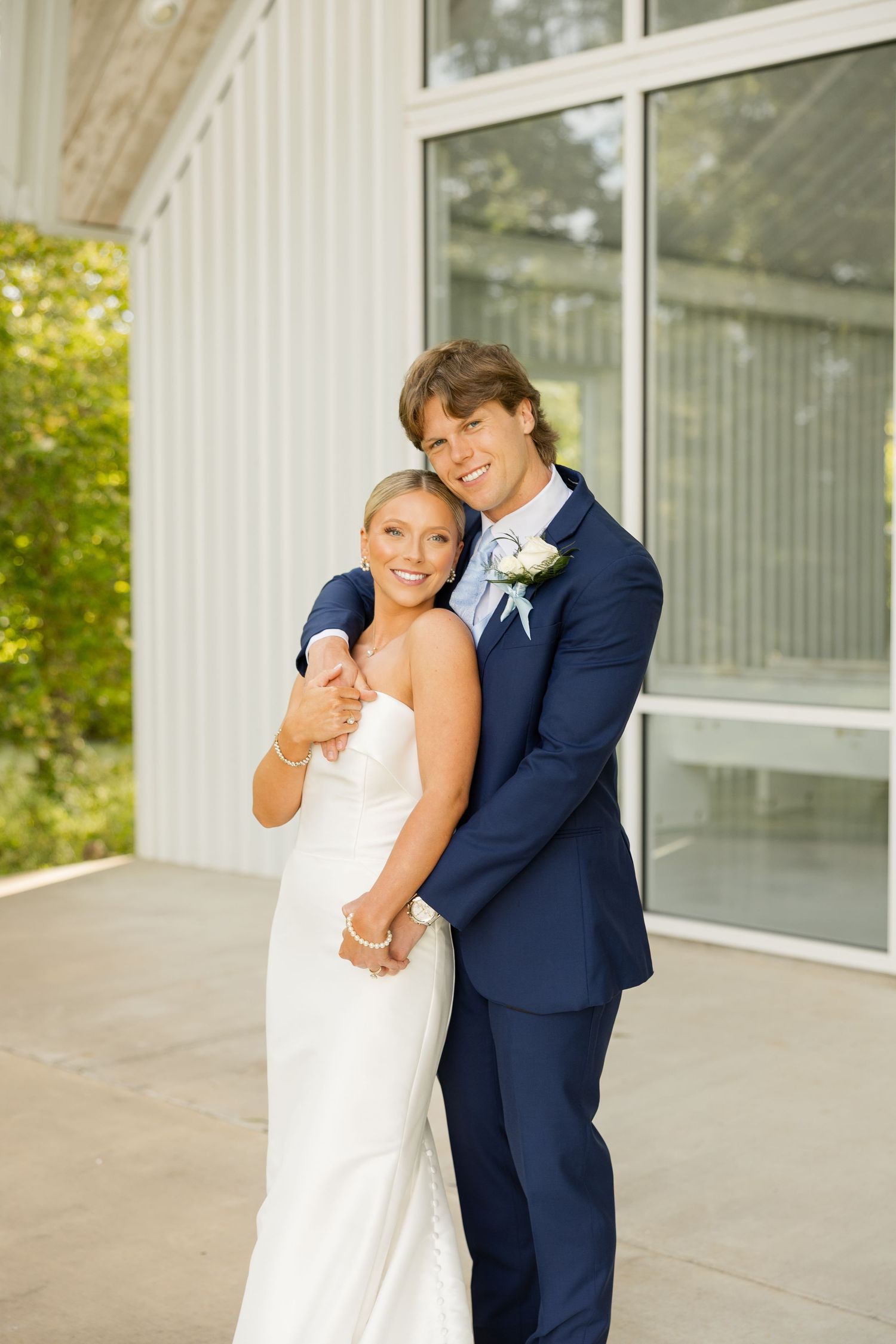 A romantic embrace outside a modern white chapel on a sunny wedding day.Cold Springs Events