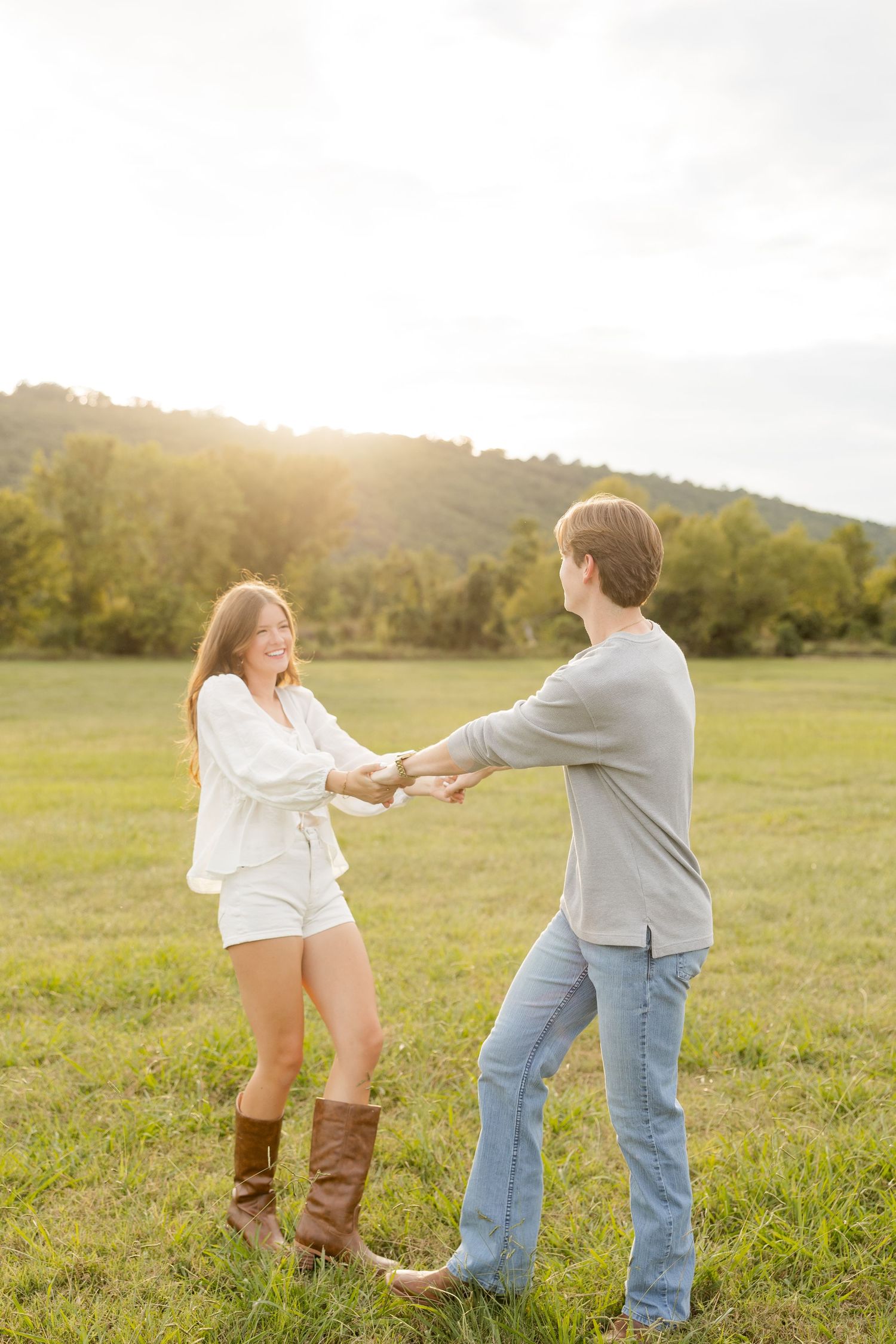 A playful couple dances together in a sunlit field during golden hour.