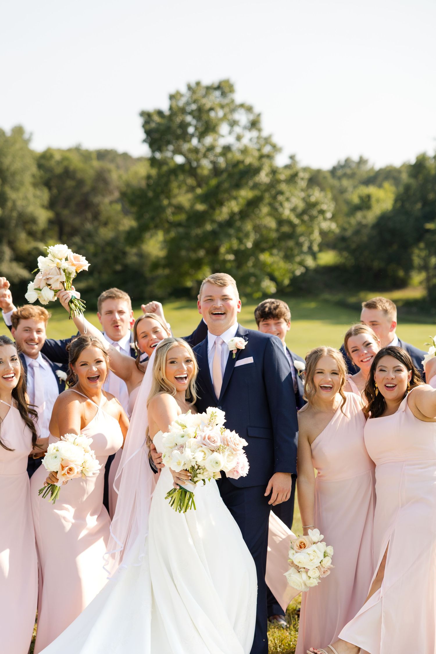 Wedding party in navy suits and blush pink dresses laughing joyfully outdoors. Sassafras Vineyards