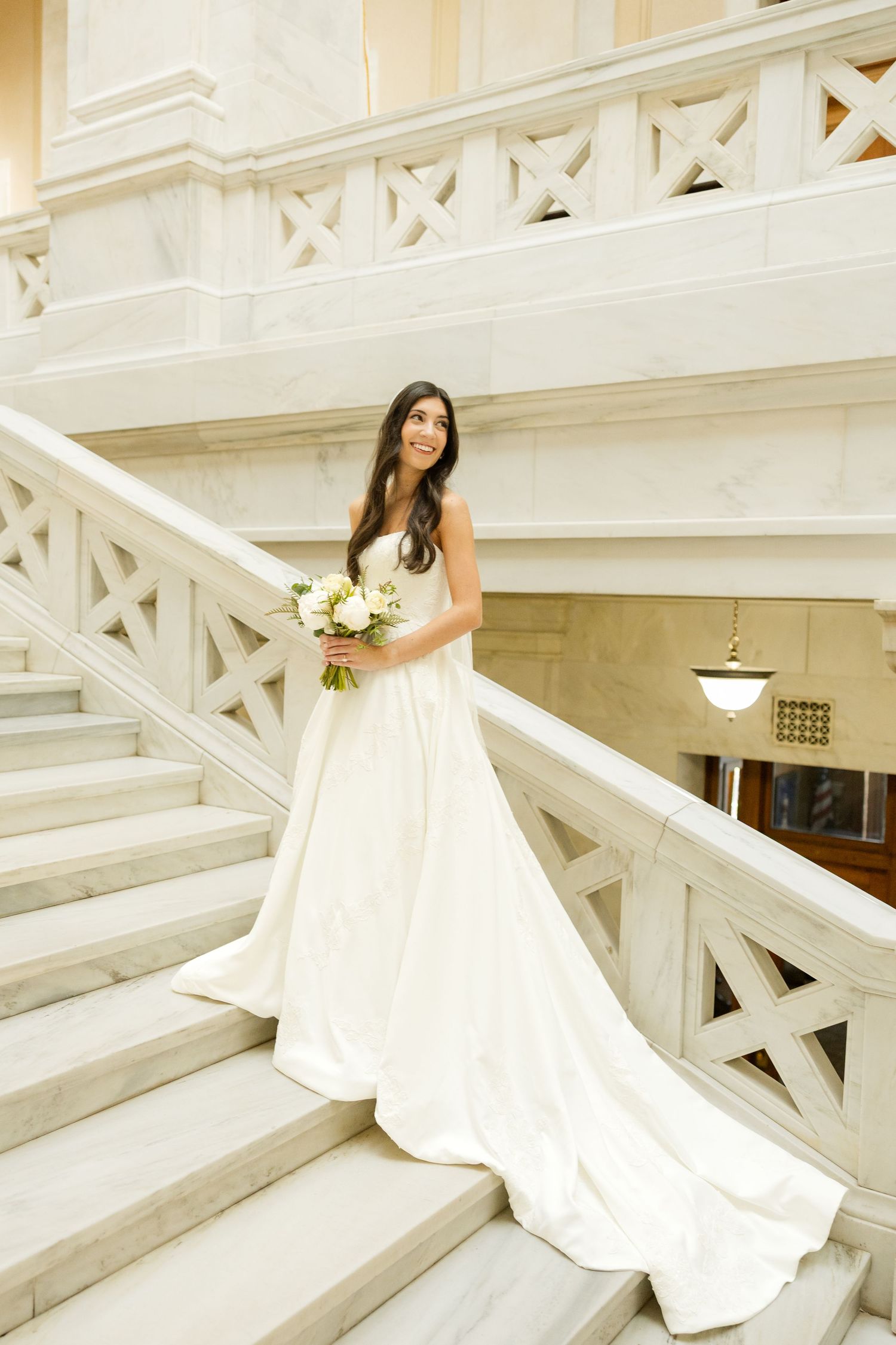 A stunning white wedding gown cascades down elegant white marble stairs in a series of artistic bridal portraits.